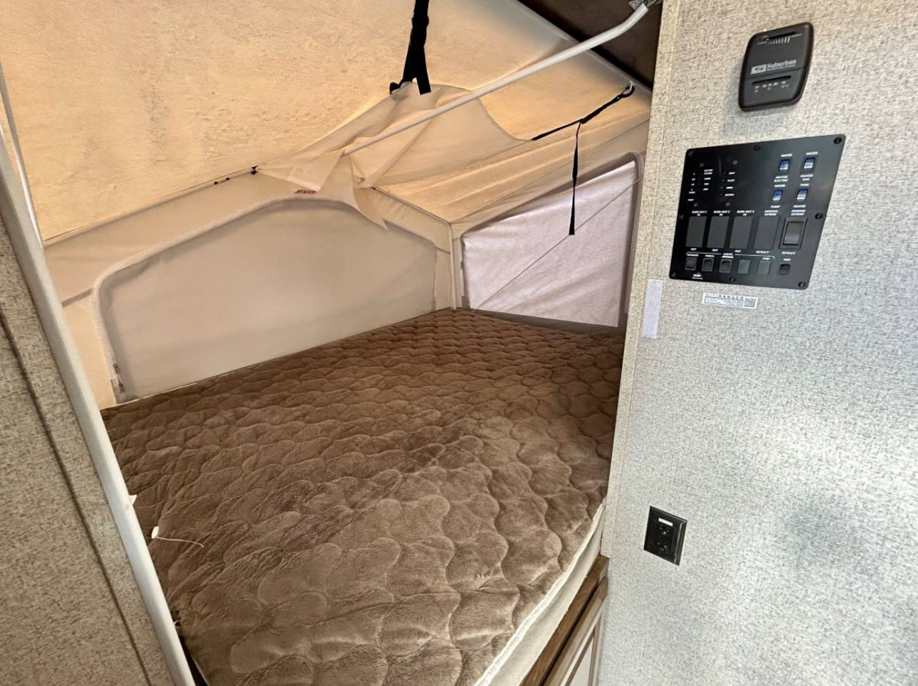 Inside an RV rental, a pop-out bed with quilted mattress and interior control panel. Perfect camper sleeping space.. Forest River Rockwood Roo 2019
