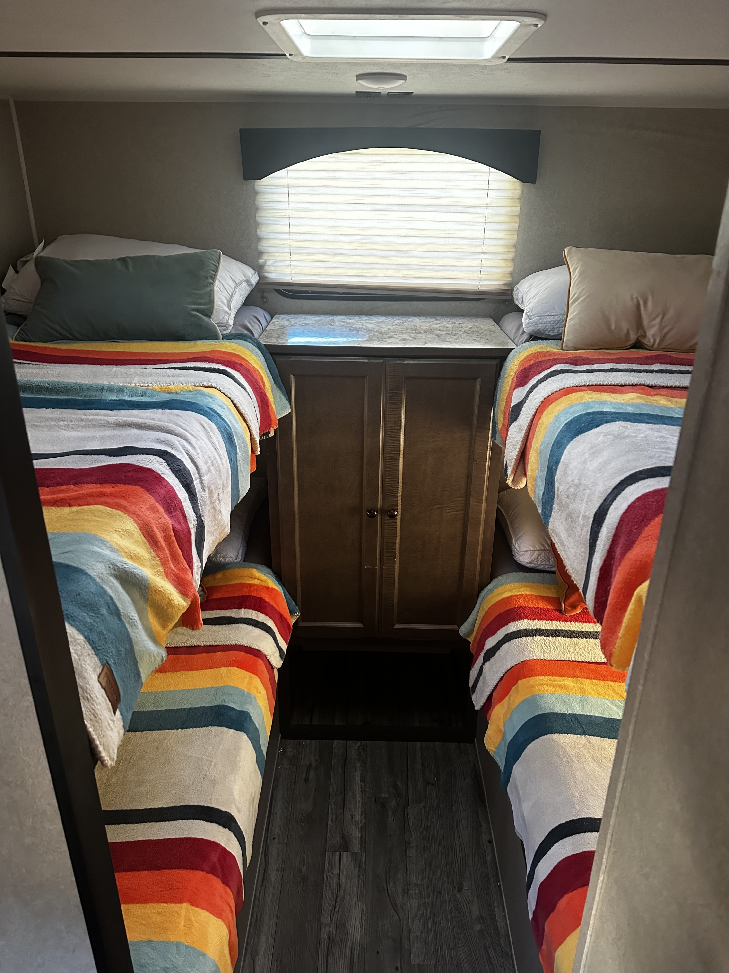 Cozy RV rental: Four bunk beds with vibrant striped blankets and a central cabinet, perfect for family travel.. Sunset Park RV Sun Lite 2020