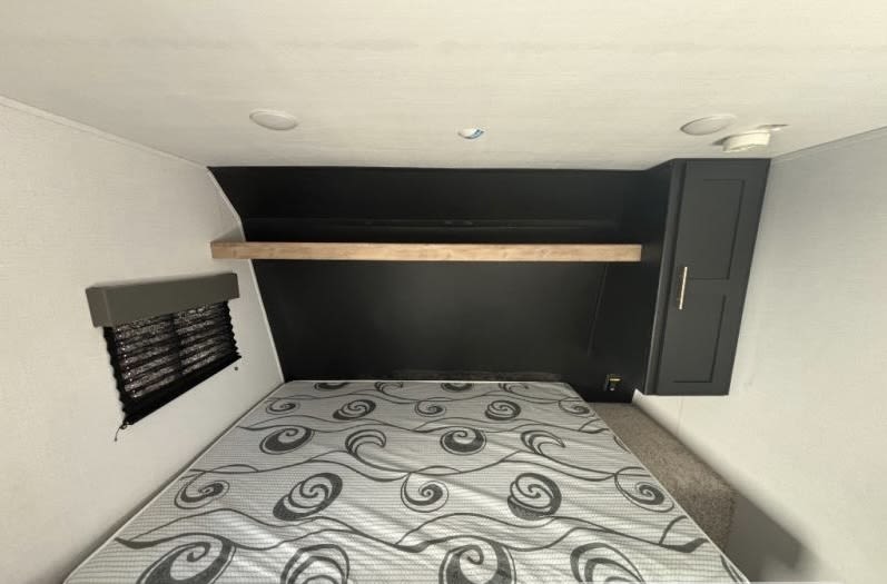This RV rental bedroom features a comfy bed, a black headboard with a shelf, a window, and a cabinet.. Keystone RV Springdale 2023