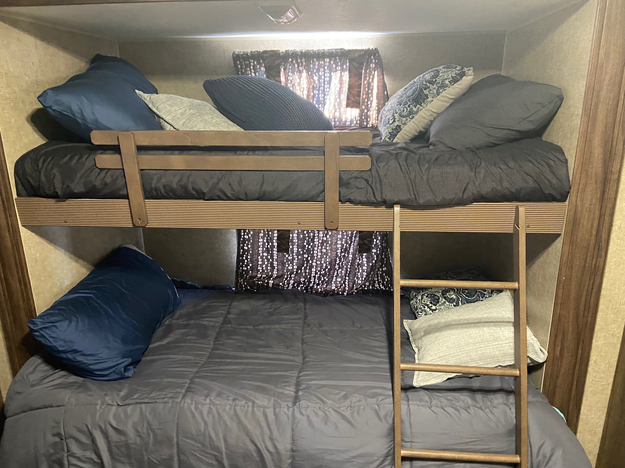 Inside this RV rental, two bunk beds are neatly made with dark bedding and assorted pillows, featuring a wooden ladder for access.. KZ Sportsman 2015