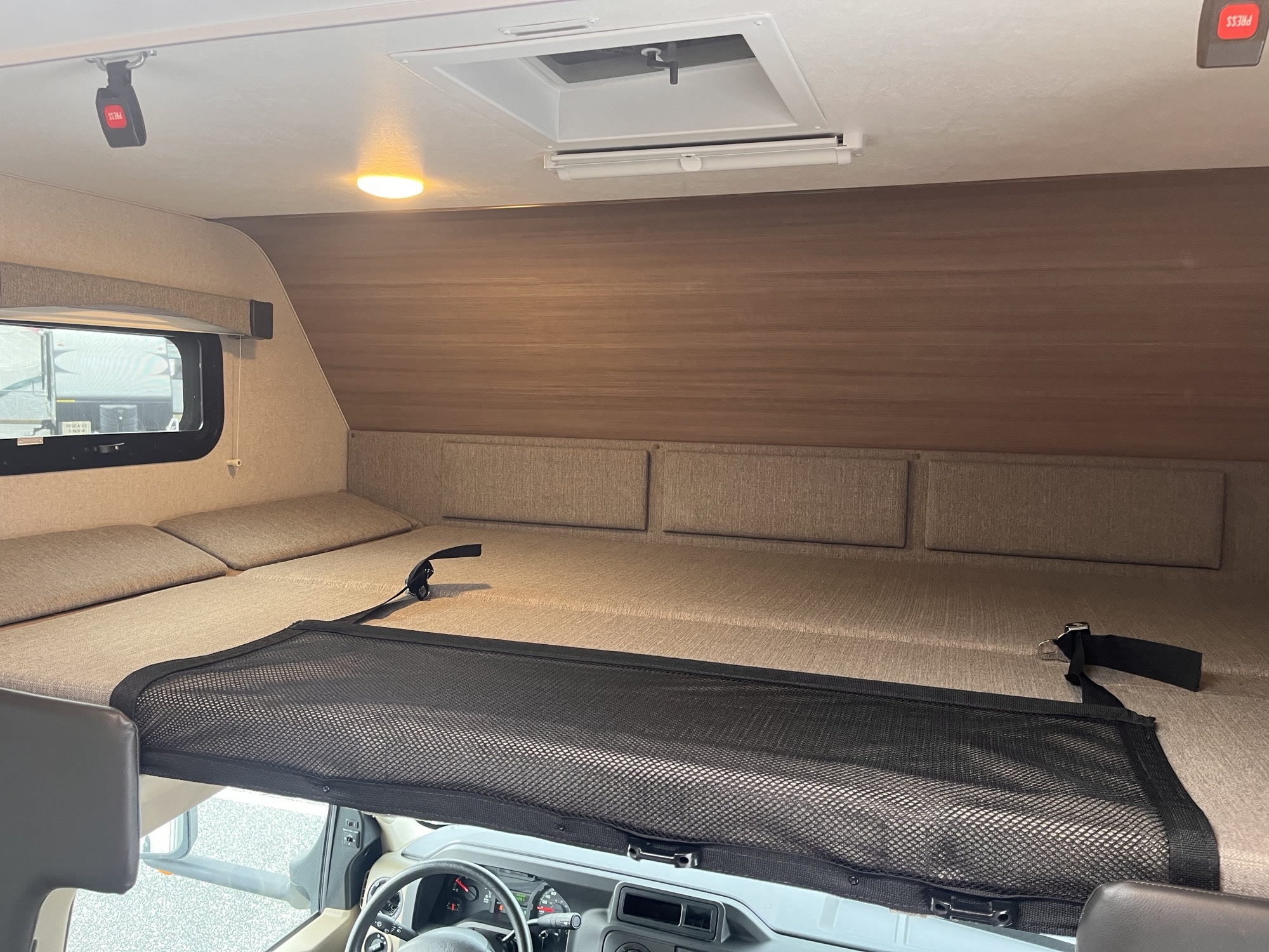 Inside an RV rental: a cozy cab-over bunk bed with a safety net, window, and ceiling light for comfortable travels.. Ford Adventurer 2021