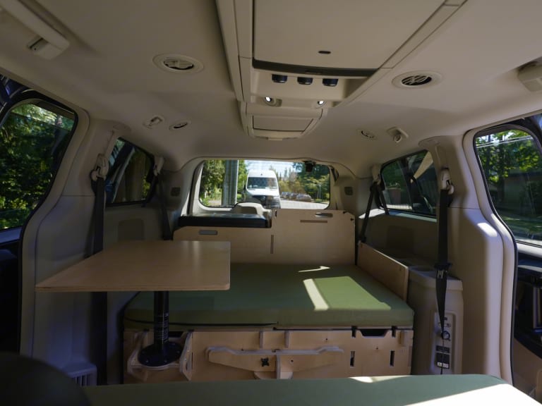 Inside an RV rental, this custom minivan conversion offers a comfortable bed and adjustable table for travelers.. Dodge Caravan 2016
