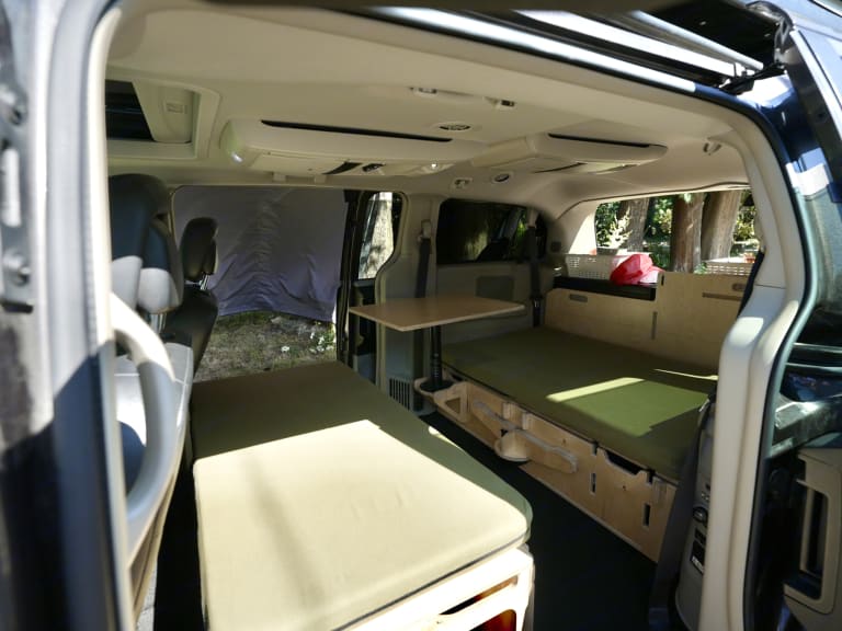 Cozy camper van conversion interior, perfect for an rv rental adventure. Features comfortable beds, table, and storage for glamping.. Dodge Caravan 2016