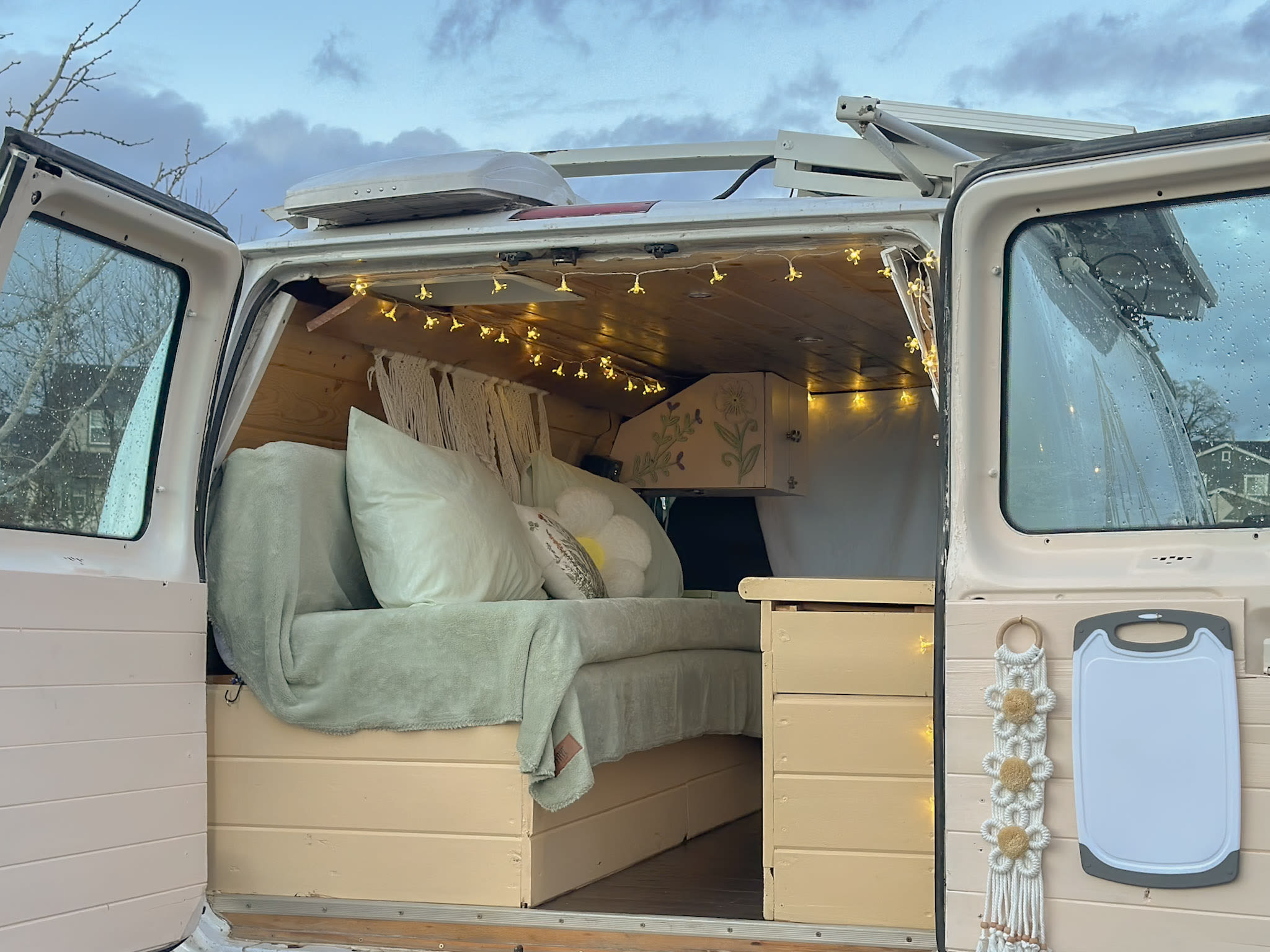 Interior of a cozy, custom-built camper van, showing a bed with pillows, string lights, and storage. Ideal for rv rental.. Ford Econoline E250supercab 2006