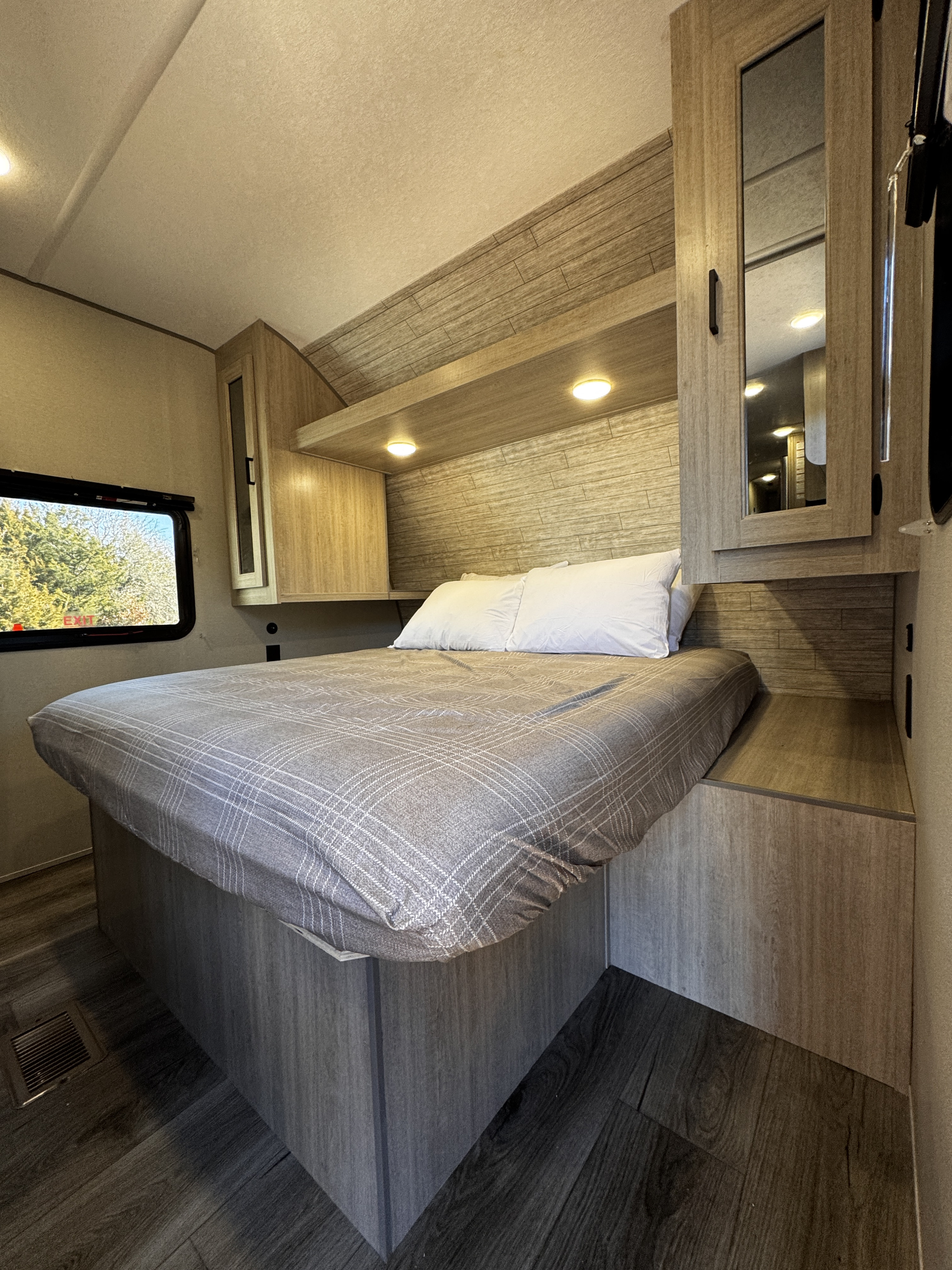 Cozy RV rental bedroom with a bed, plaid comforter, wood cabinetry, and a window view of trees outside.. Coachmen Catalina Summit Series 8 261BHS 2025