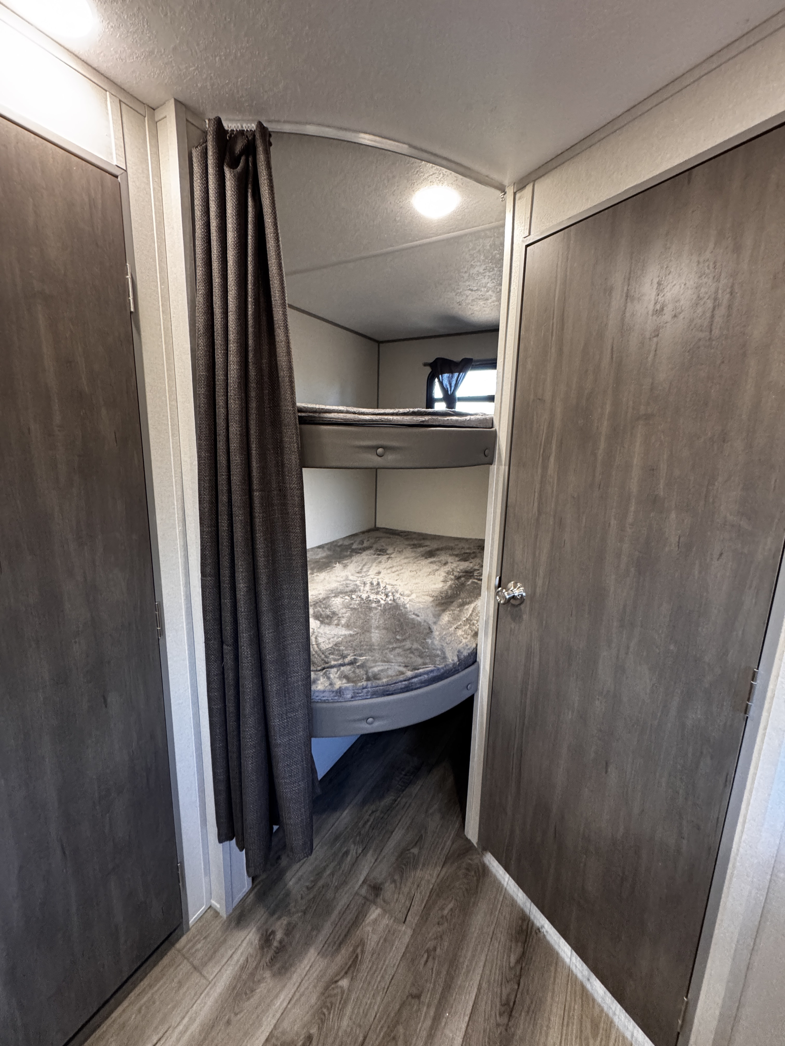 Cozy RV rental interior featuring comfortable bunk beds with grey bedding, a privacy curtain, and wood-look flooring.. Coachmen Catalina Summit Series 8 261BHS 2025