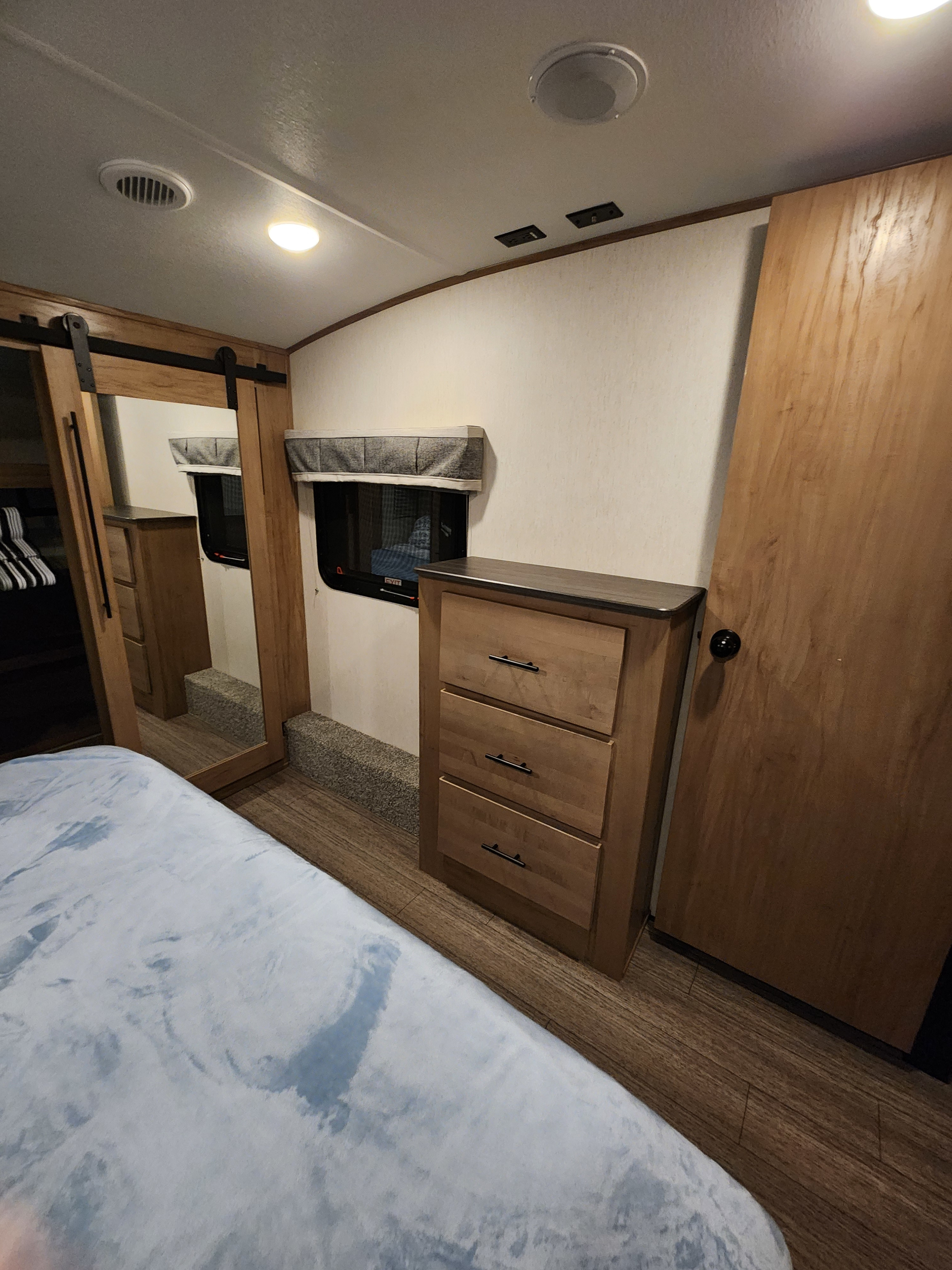 Inside an RV rental bedroom: bed with light blue bedding, wooden dresser, and space-saving mirrored barn door closet.. Forest River Sabre 2023