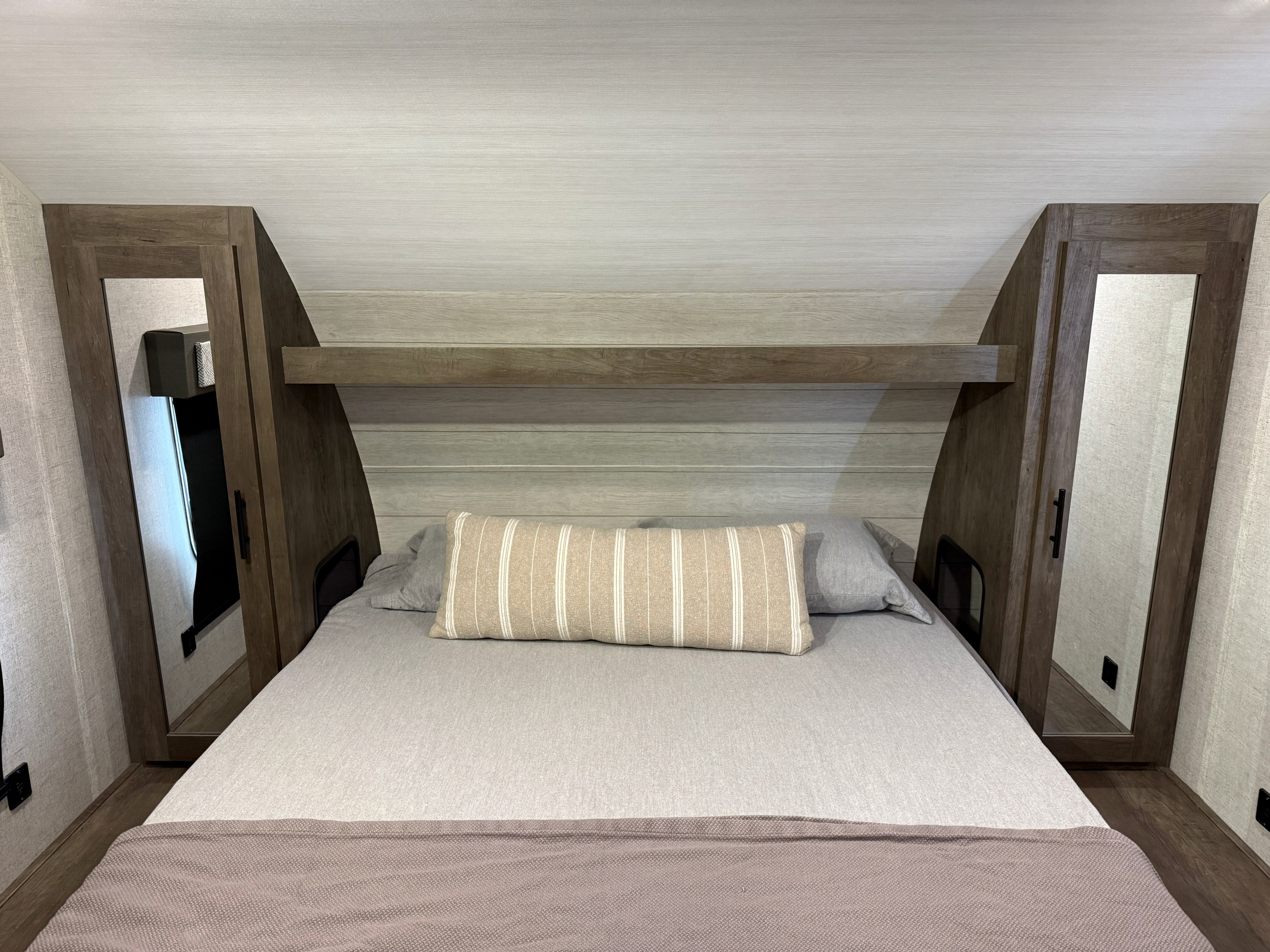 This RV rental bedroom features a comfortable bed, light wood finishes, an overhead shelf, and mirrored storage.. Forest River Wildwood X-Lite 2020