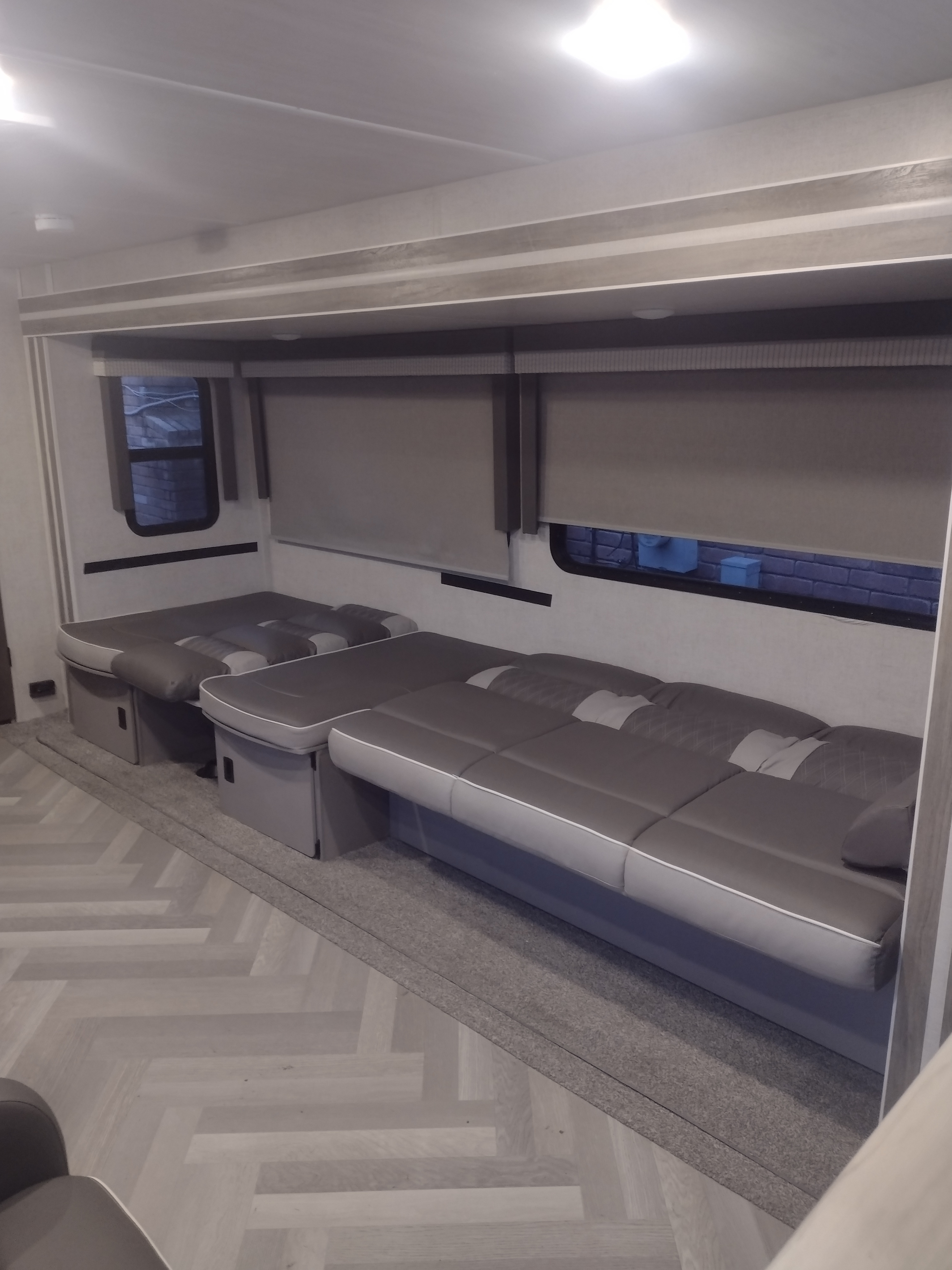 RV rental interior showcasing modern gray seating that converts to beds, sleek window blinds, and light herringbone floors.. Forest River Wildwood 2021