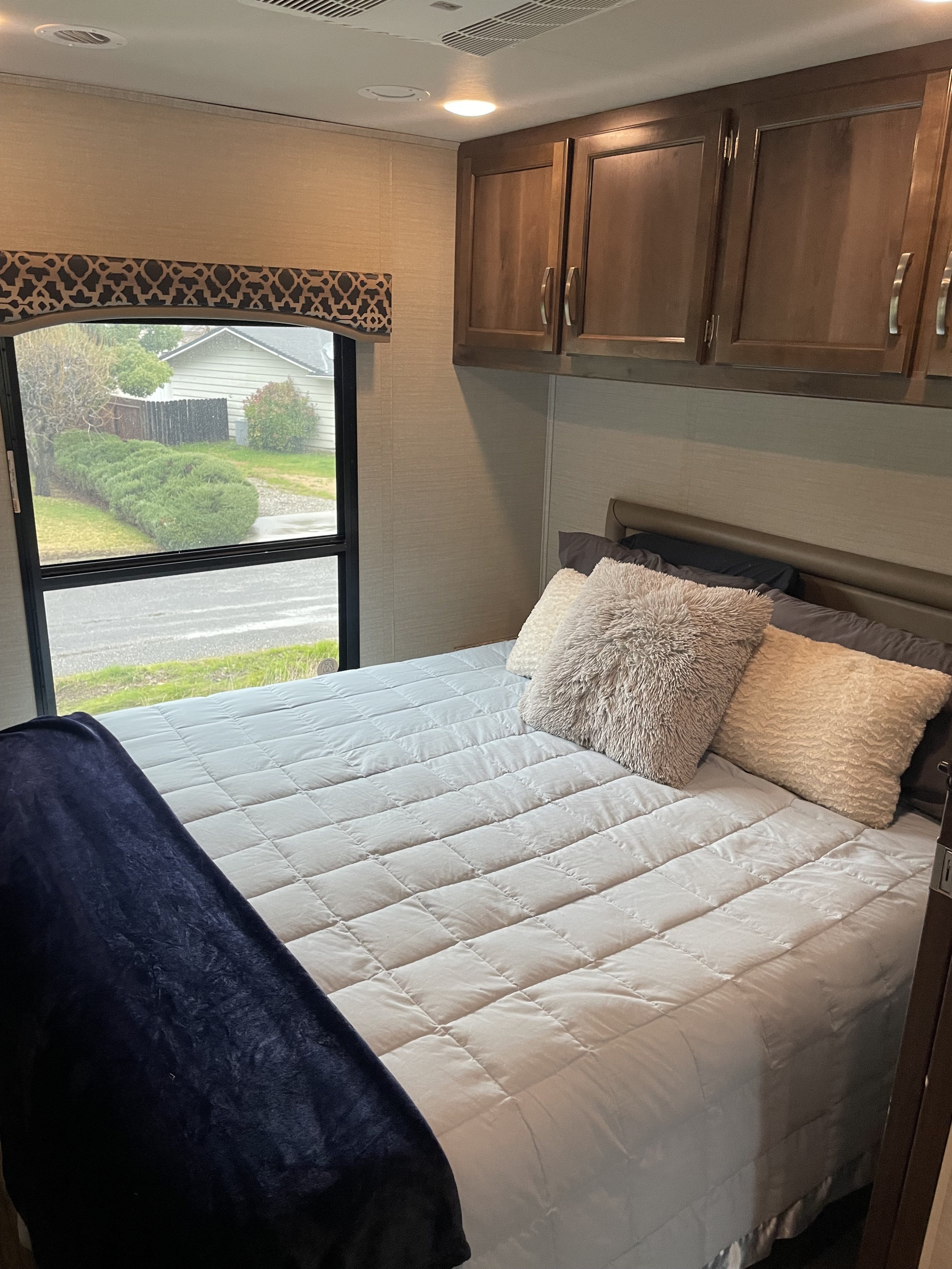 Cozy RV rental bedroom featuring a queen bed with quilted comforter, fluffy pillows, dark cabinets, and a window with an outdoor view.. Jayco Alante 2018
