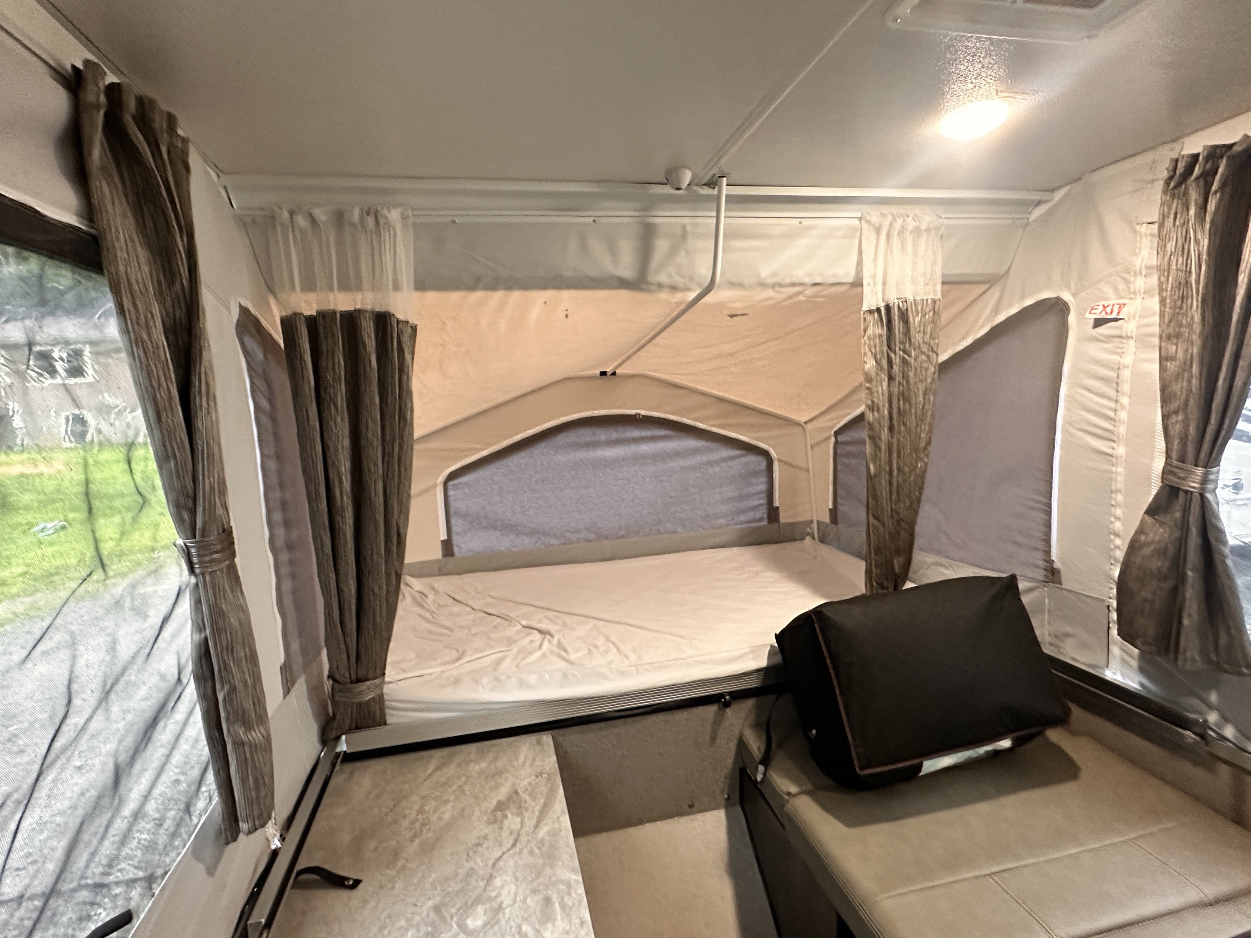 Inside a compact pop-up RV rental: a comfortable bed, window views through mesh, side curtains, and an exit sign.. Forest River Rockwood Freedom 2020