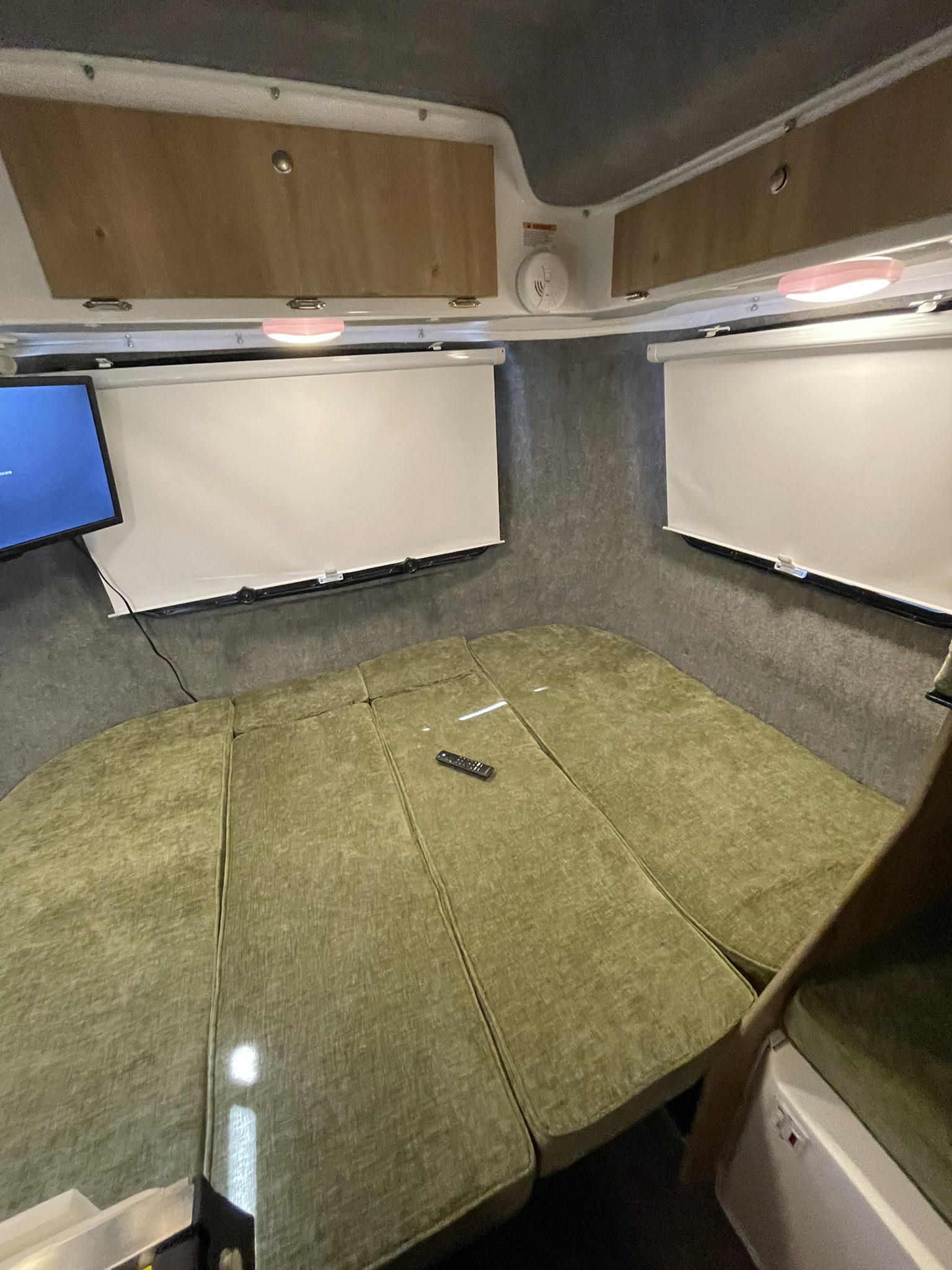 RV rental interior: A green modular bed fills the space, flanked by a TV, shades, and overhead storage for a cozy stay.. Casita 17 Heritage Deluxe 2025