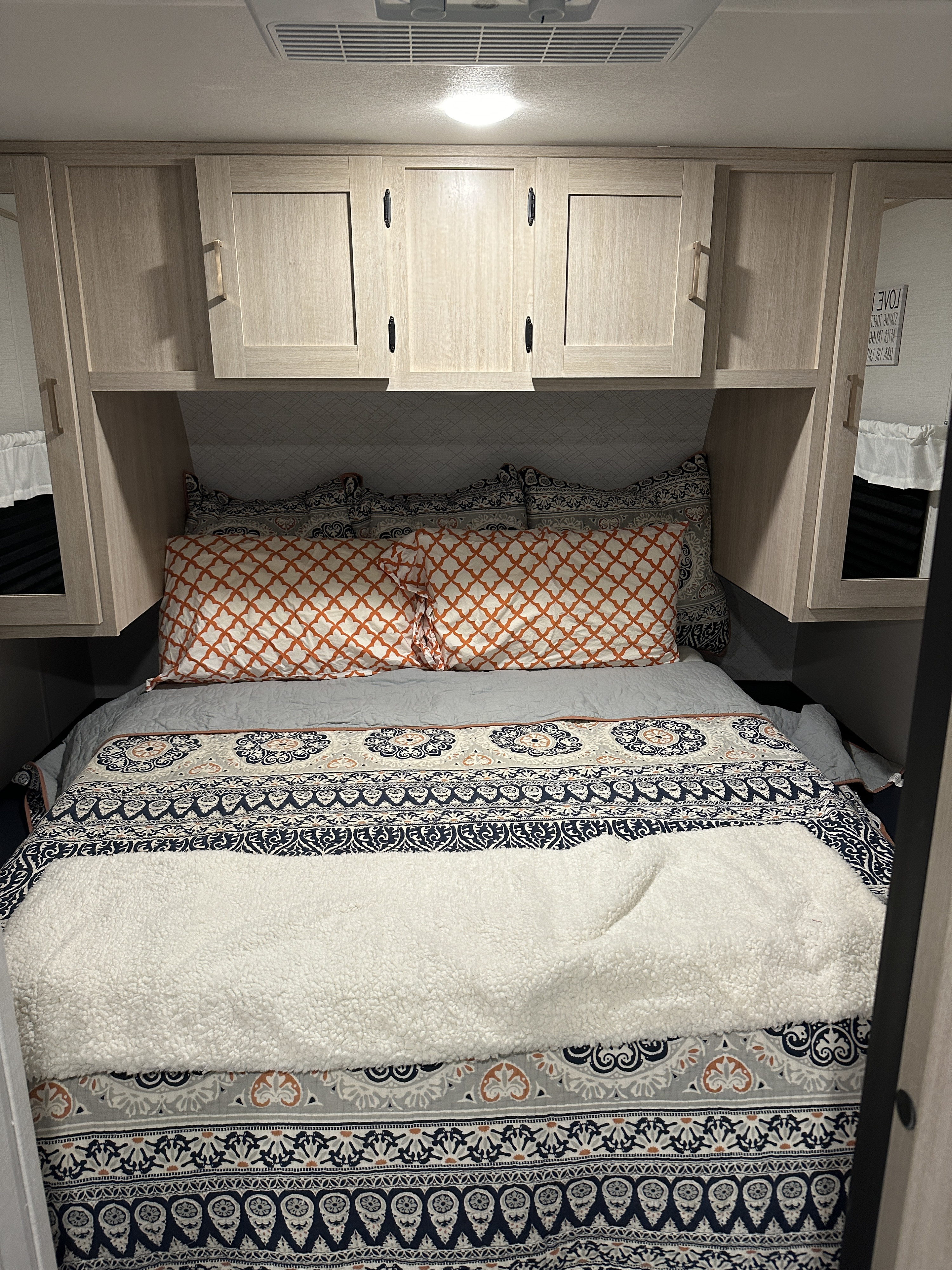 Cozy RV rental bedroom featuring patterned bedding, orange pillows, and functional overhead storage cabinets.. Prime Time Avenger 27DBS 2024