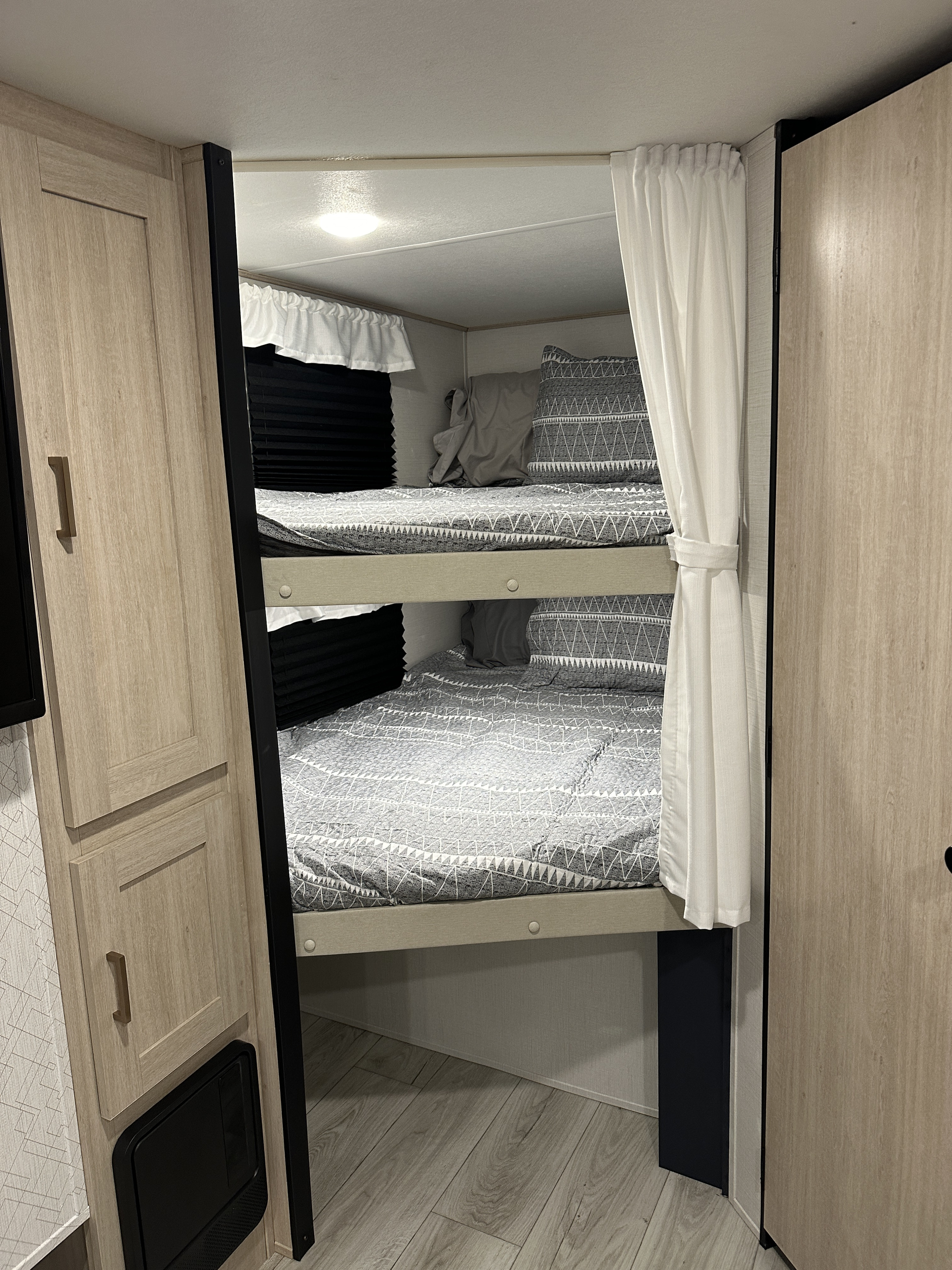 RV rental interior: Two stacked bunk beds with geometric grey bedding & white privacy curtains.. Prime Time Avenger 27DBS 2024