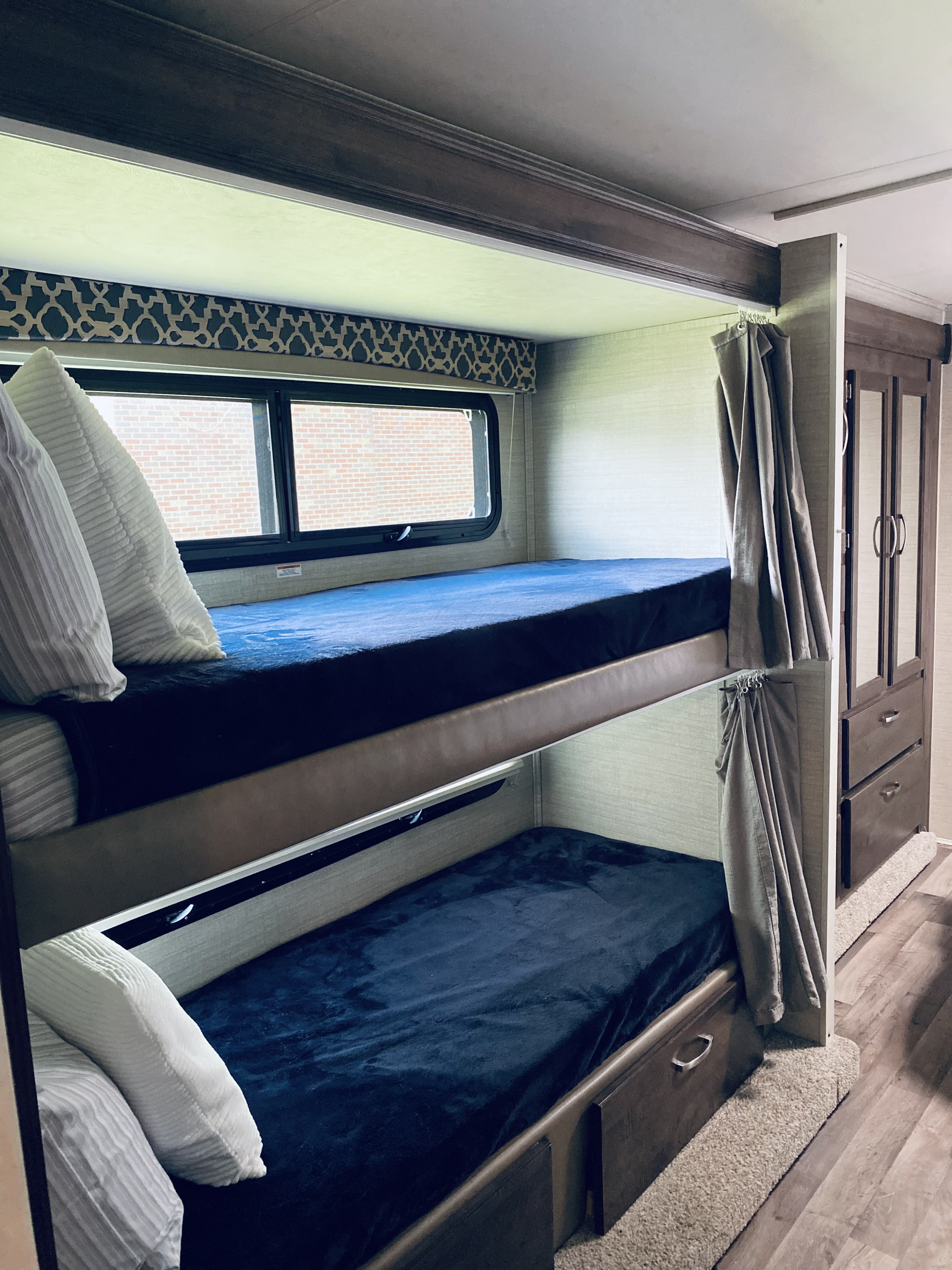 Comfortable bunk beds inside an RV rental, with blue bedding, pillows, and a window view for travelers.. Jayco Redhawk 2019