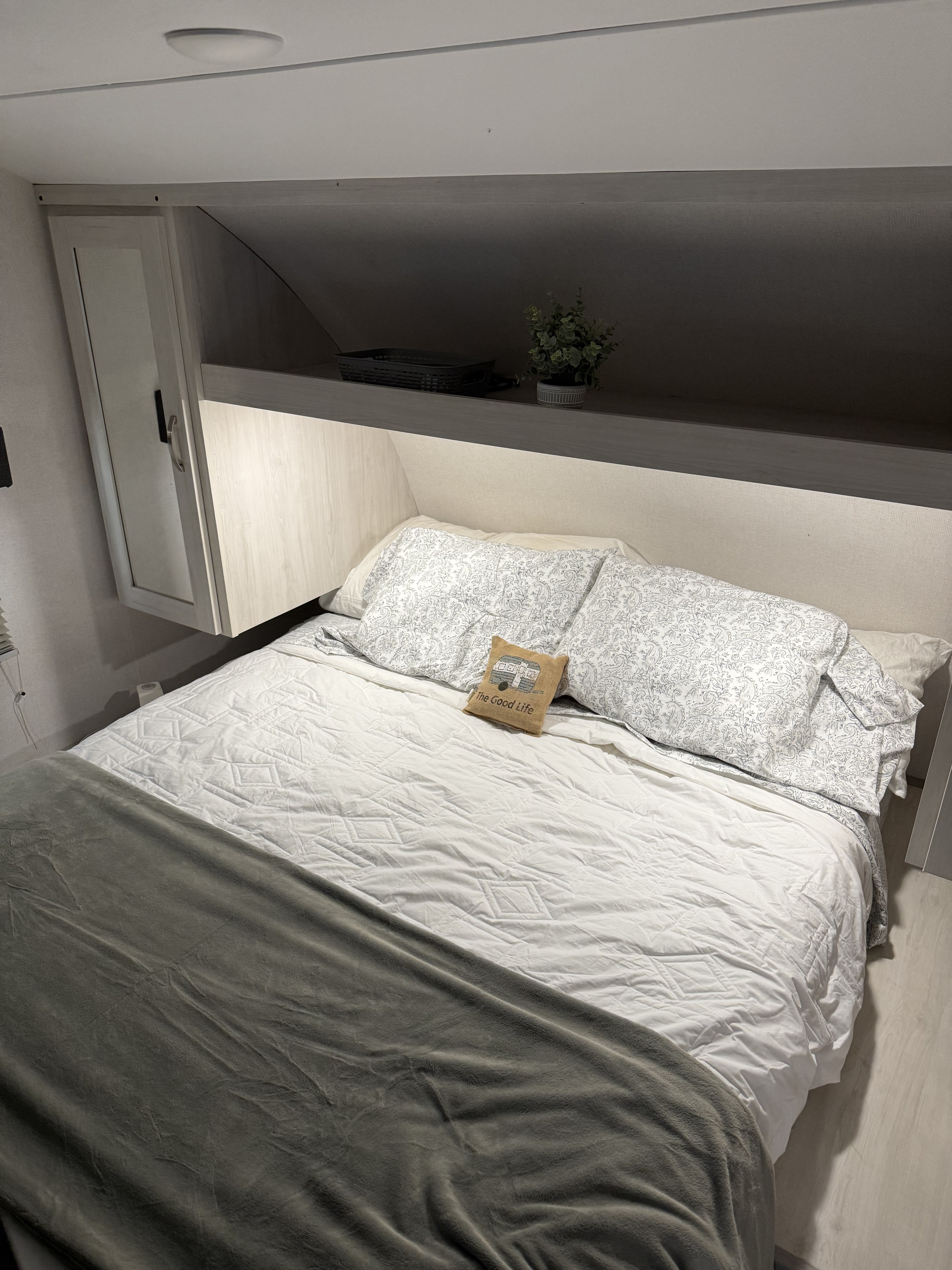 Cozy RV rental bedroom featuring a comfortable bed with patterned pillows, overhead storage, and a mirrored cabinet.. Forest River Tracer 2022