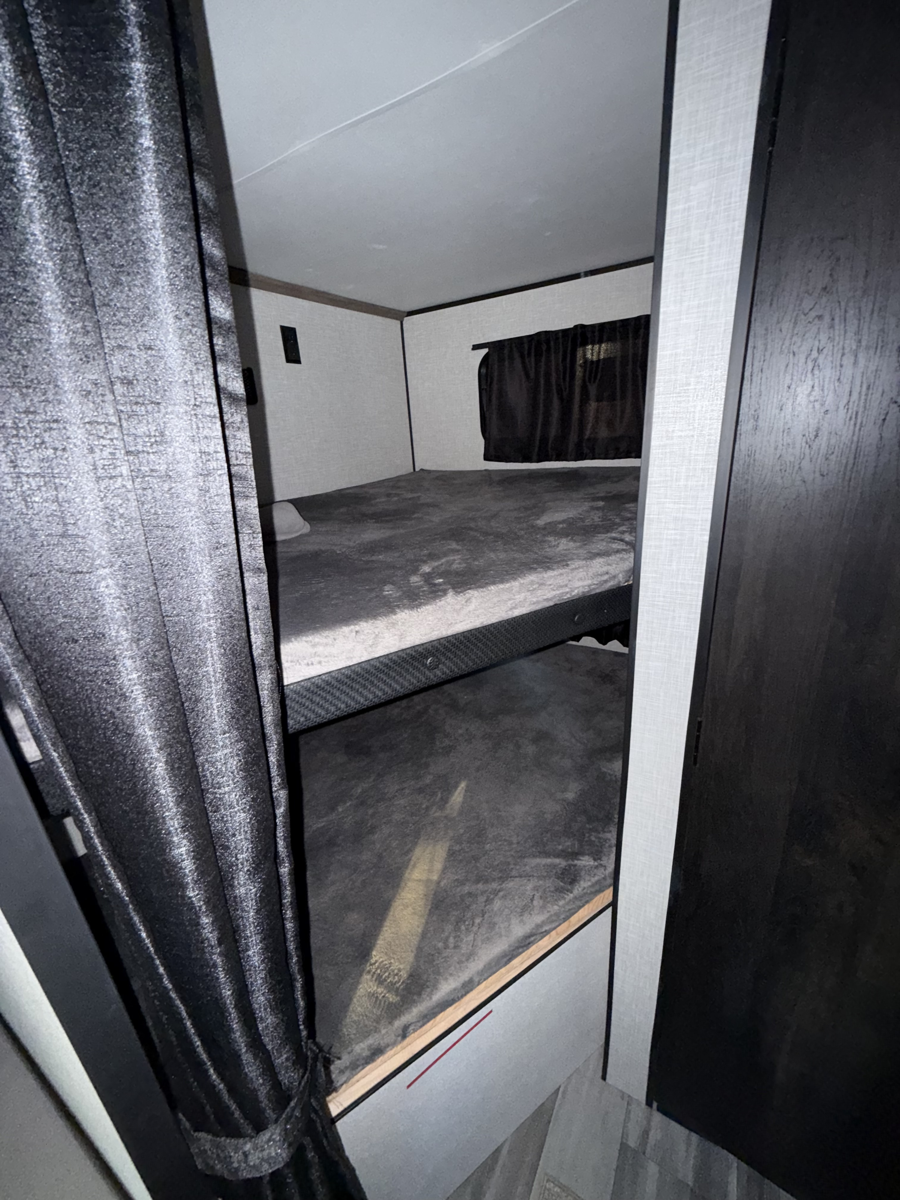 RV rental bunk beds: two dark grey beds with curtains, offering compact sleeping space for camping adventures.. Highland Ridge RV Open Range 2024