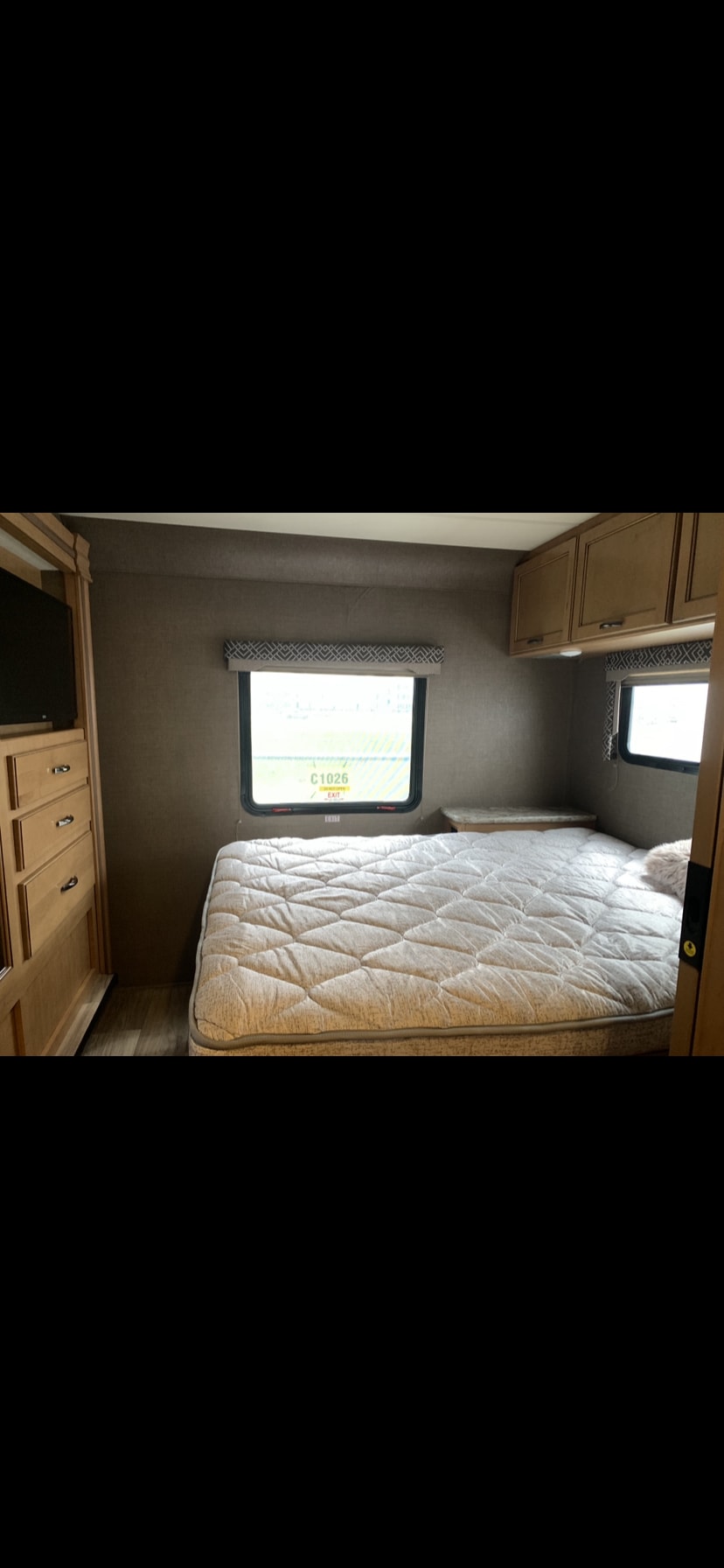RV rental bedroom interior featuring a quilted bed, two windows, and wood cabinetry with a TV mount.. Thor Four Winds 2018