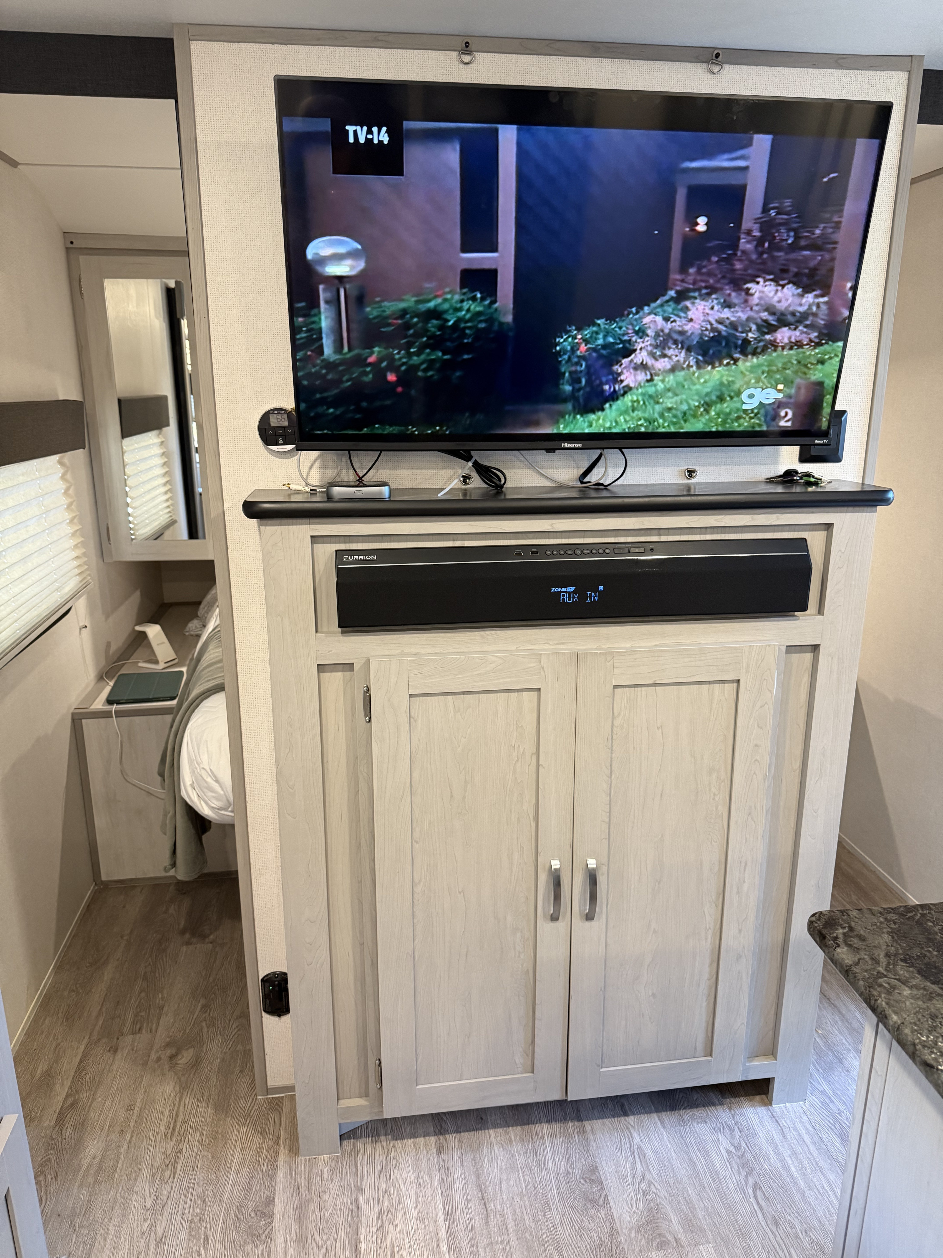 This modern RV rental features an entertainment center with a TV, soundbar, and built-in storage, facing a cozy bedroom area.. Forest River Tracer 2022