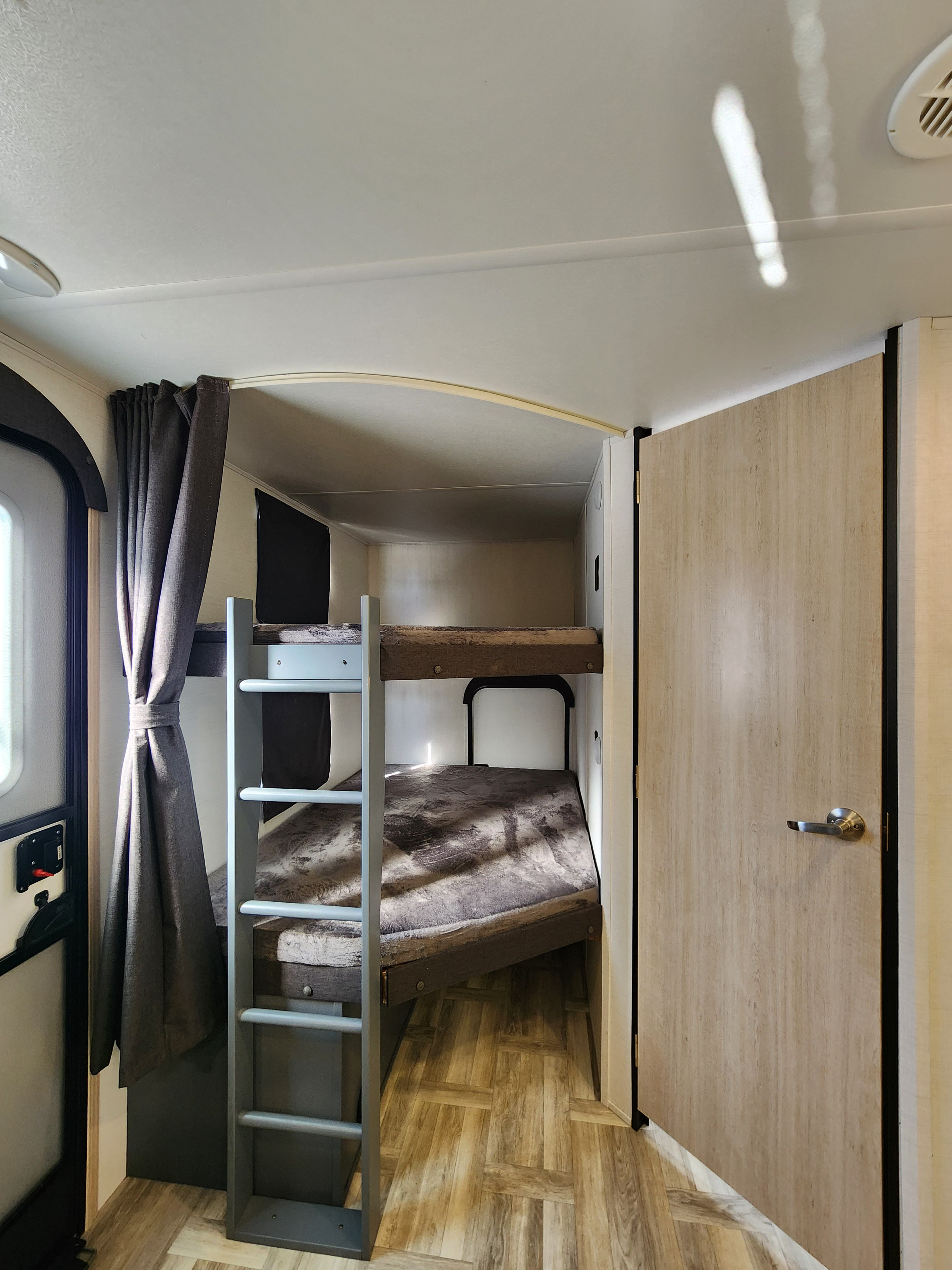 RV rental bunk beds: a compact sleeping area with privacy curtain, light wood door, and patterned floor.. primetime tracer 2024