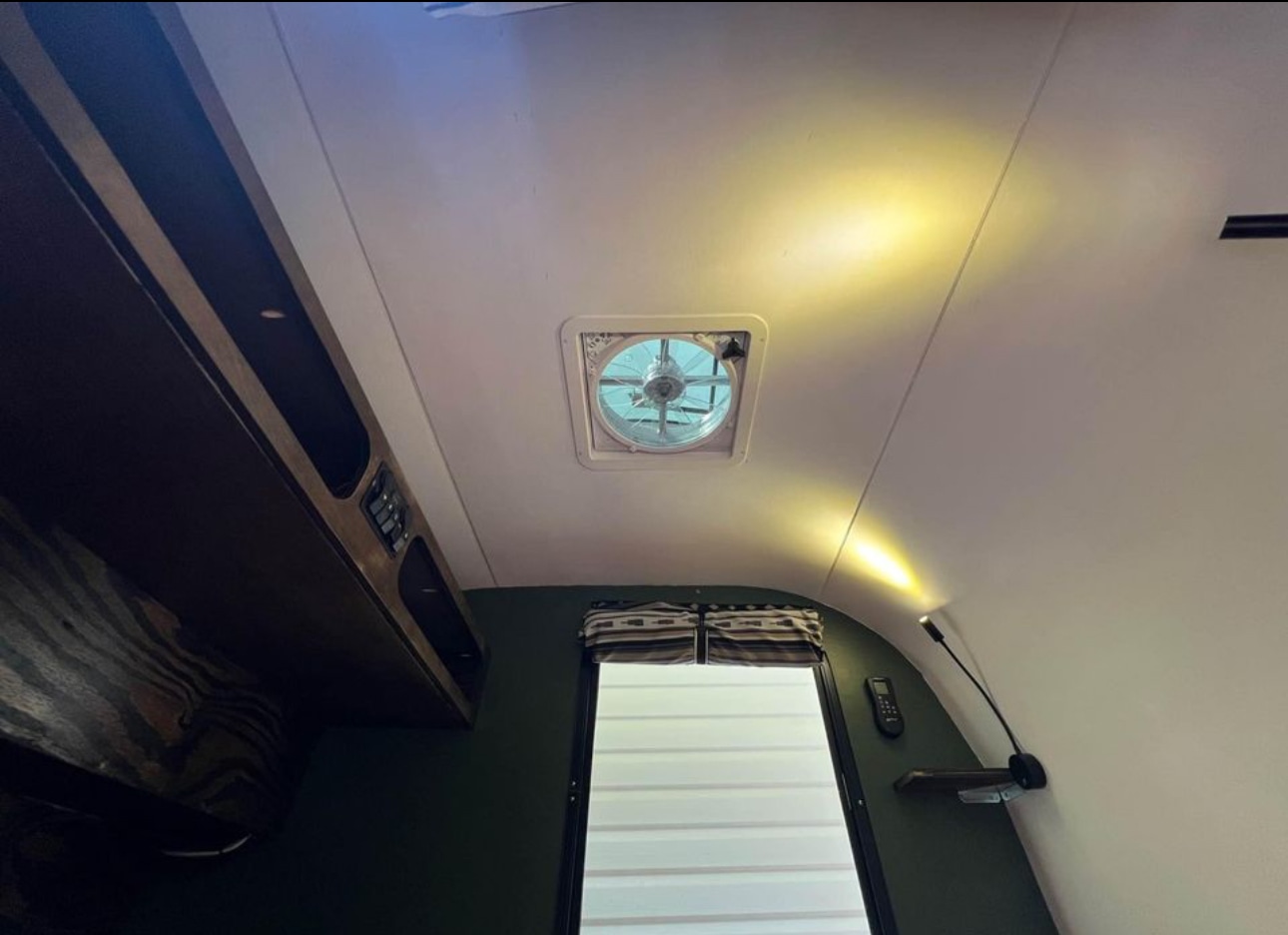 Cozy RV rental interior: visible ceiling fan, overhead storage, window, and reading lamp for comfortable living.. Other Other 2022