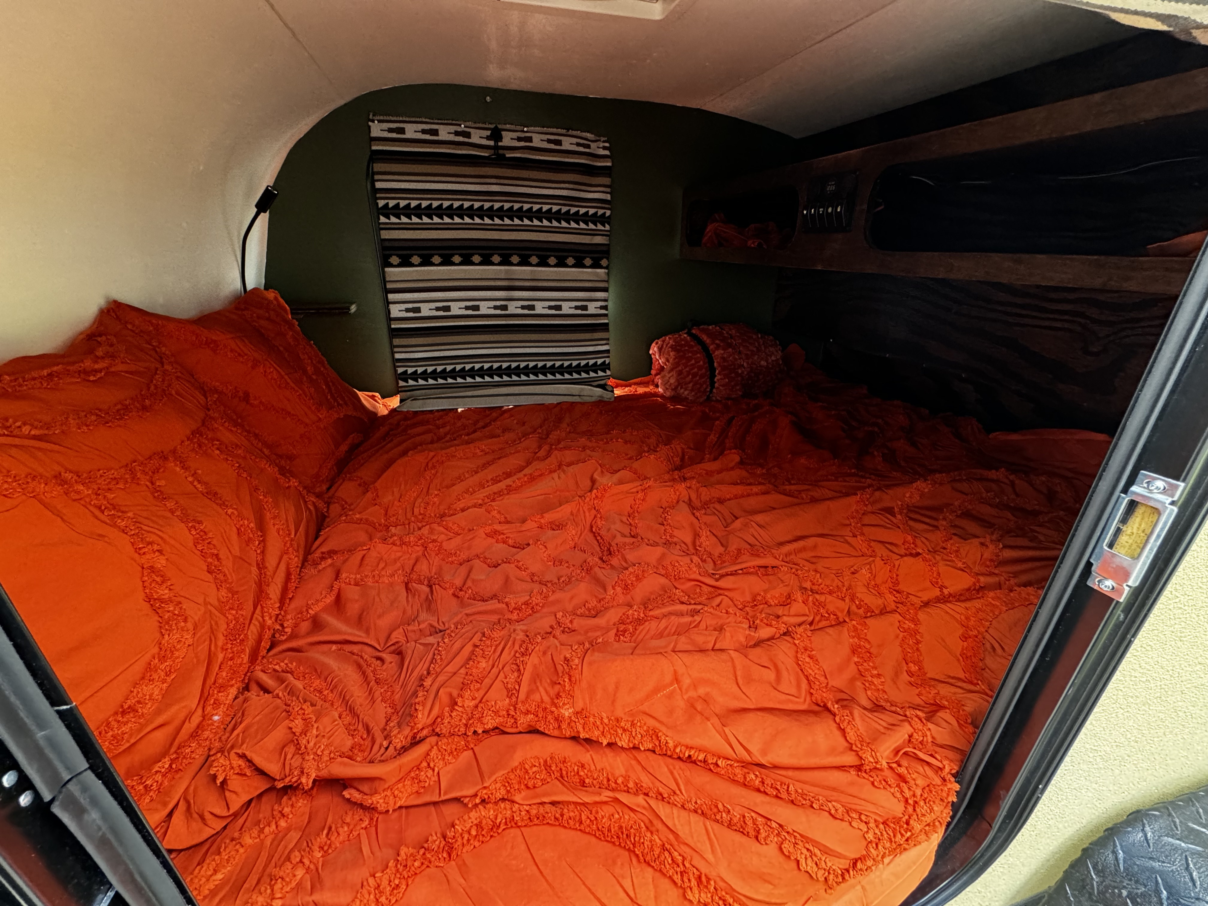 RV rental: Step into a cozy camper bedroom featuring vibrant orange bedding, a southwestern tapestry, and built-in storage.. Other Other 2022