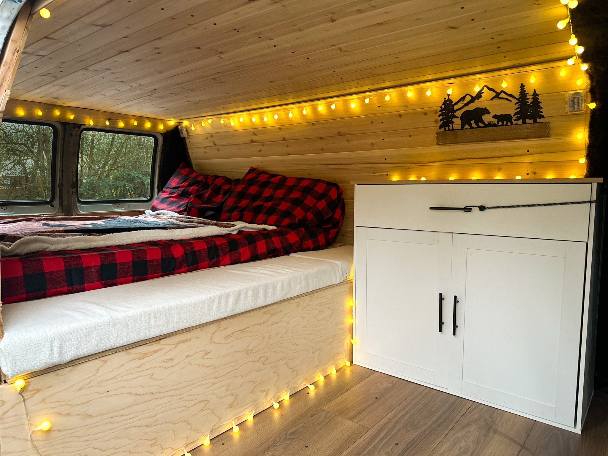 Cozy custom rv rental interior featuring wood paneling, string lights, a plaid bed, and built-in storage cabinets.. Dodge Ram Van Roadtrek 2000