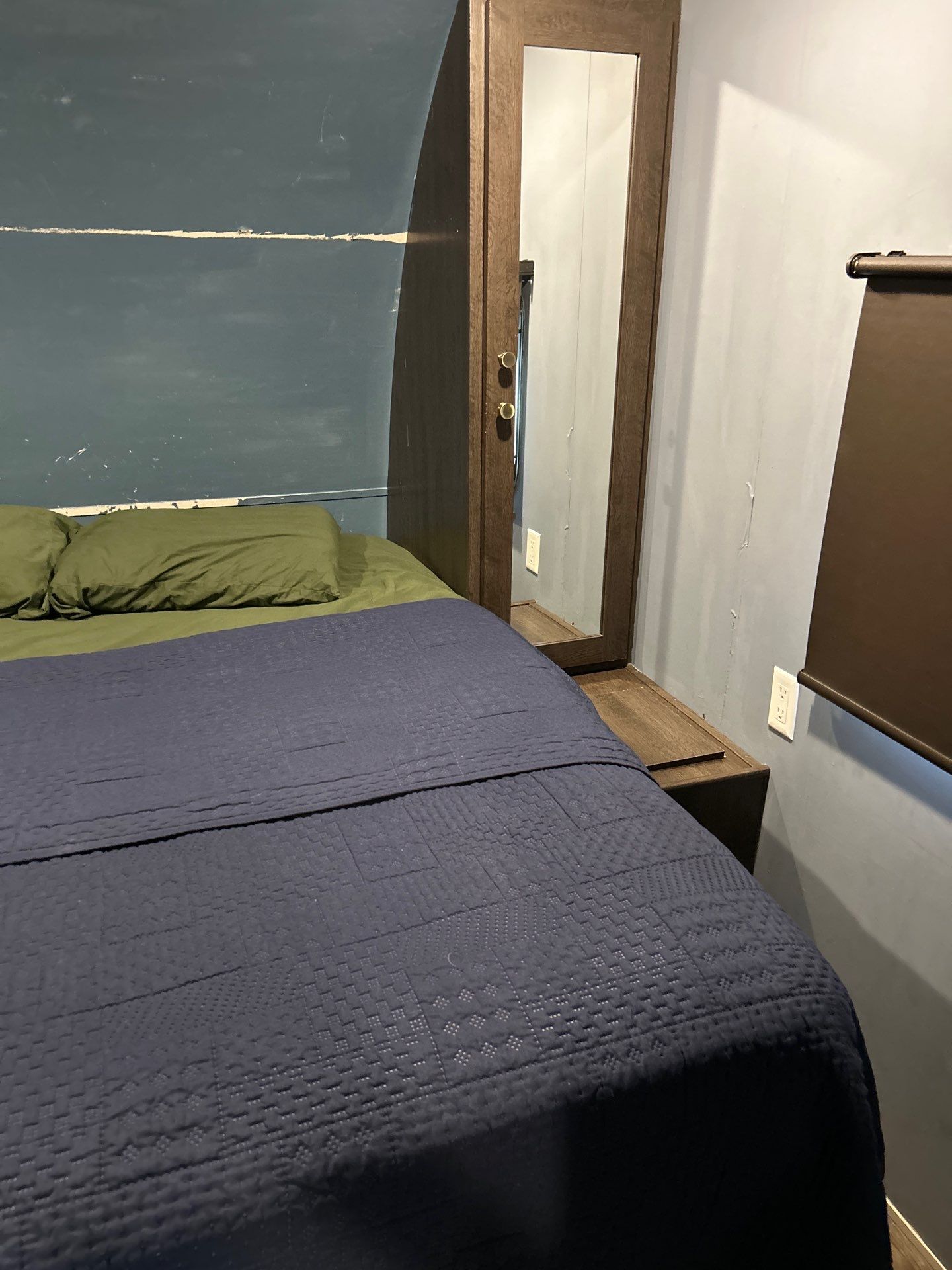 Cozy rv rental bedroom featuring a dark blue quilted bed, green pillows, and a wooden mirrored cabinet for efficient storage.. Forest River Wildwood 2019