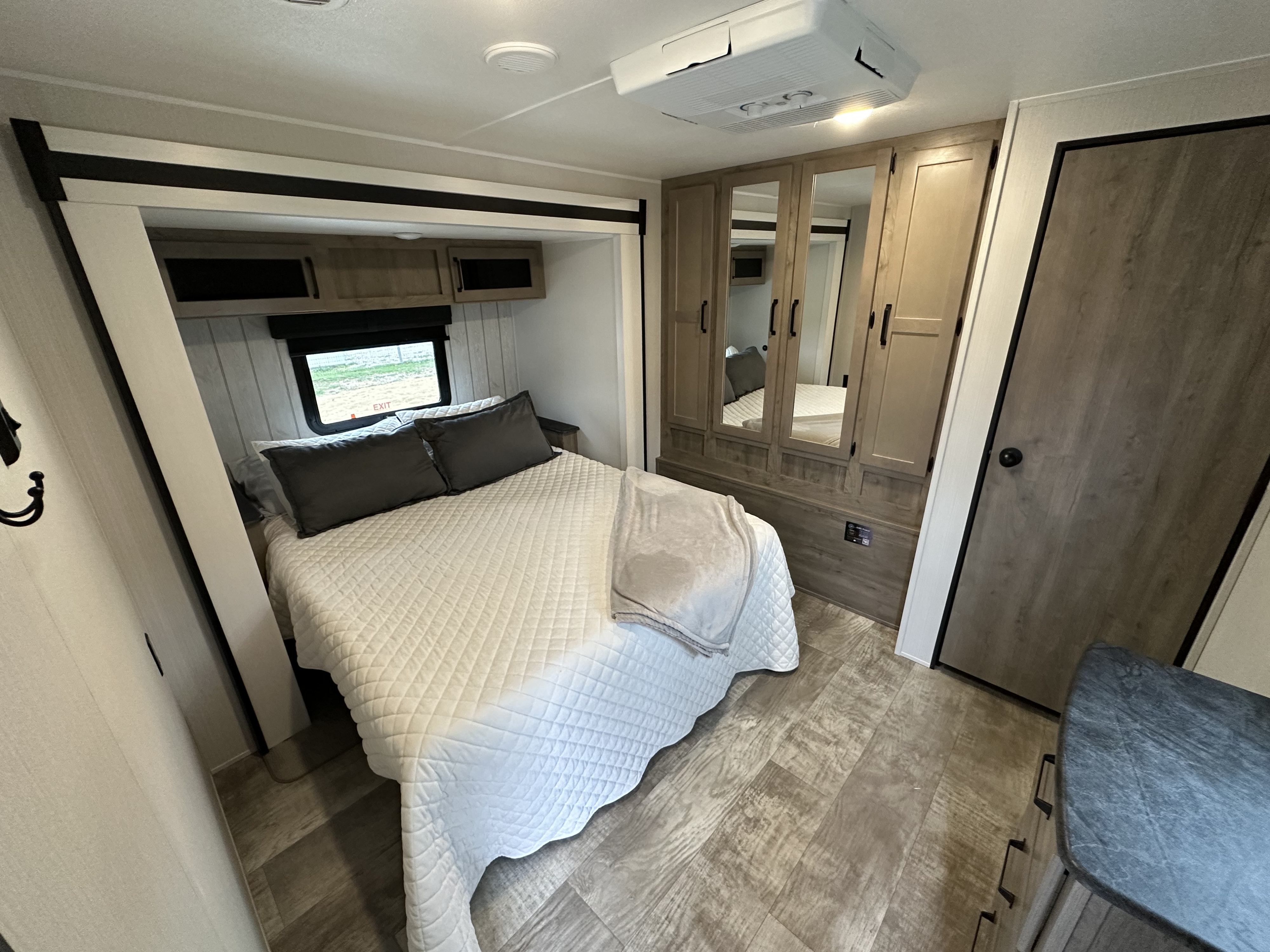 Modern RV rental bedroom featuring a comfortable bed, mirrored wardrobe, overhead storage, and wood-look flooring.. Palomino Puma 2024