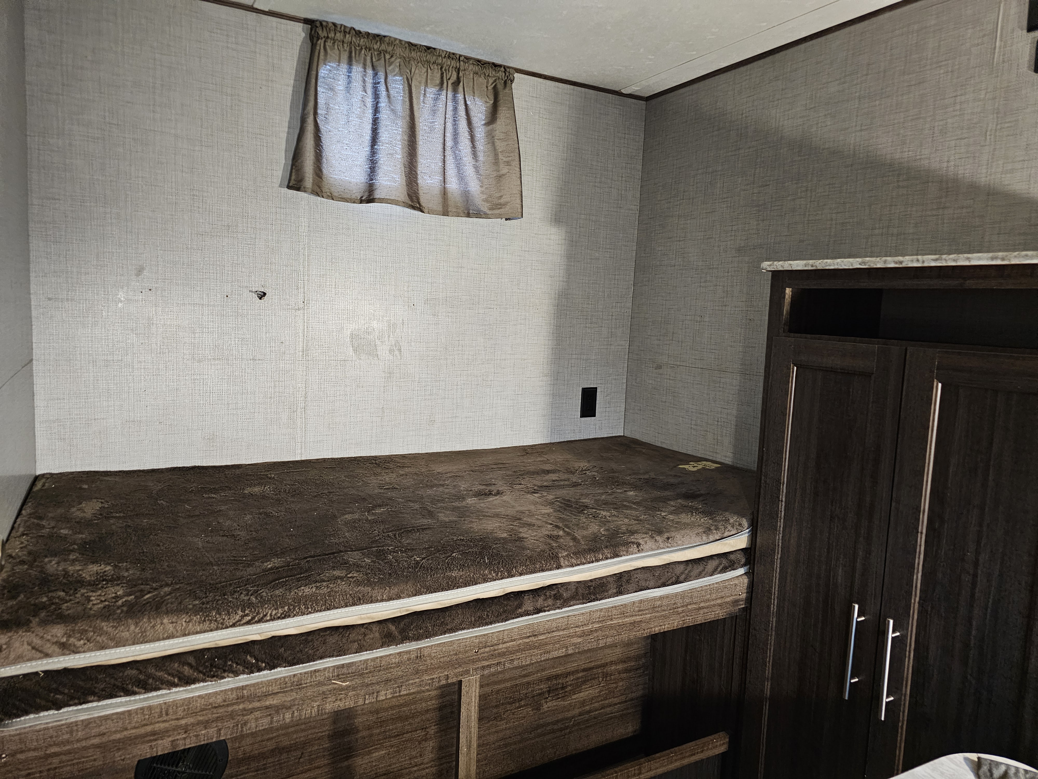 Cozy RV rental interior shows a brown plush mattress on a lower bunk bed, light textured walls, and dark wood cabinetry.. Keystone Zinger 2018