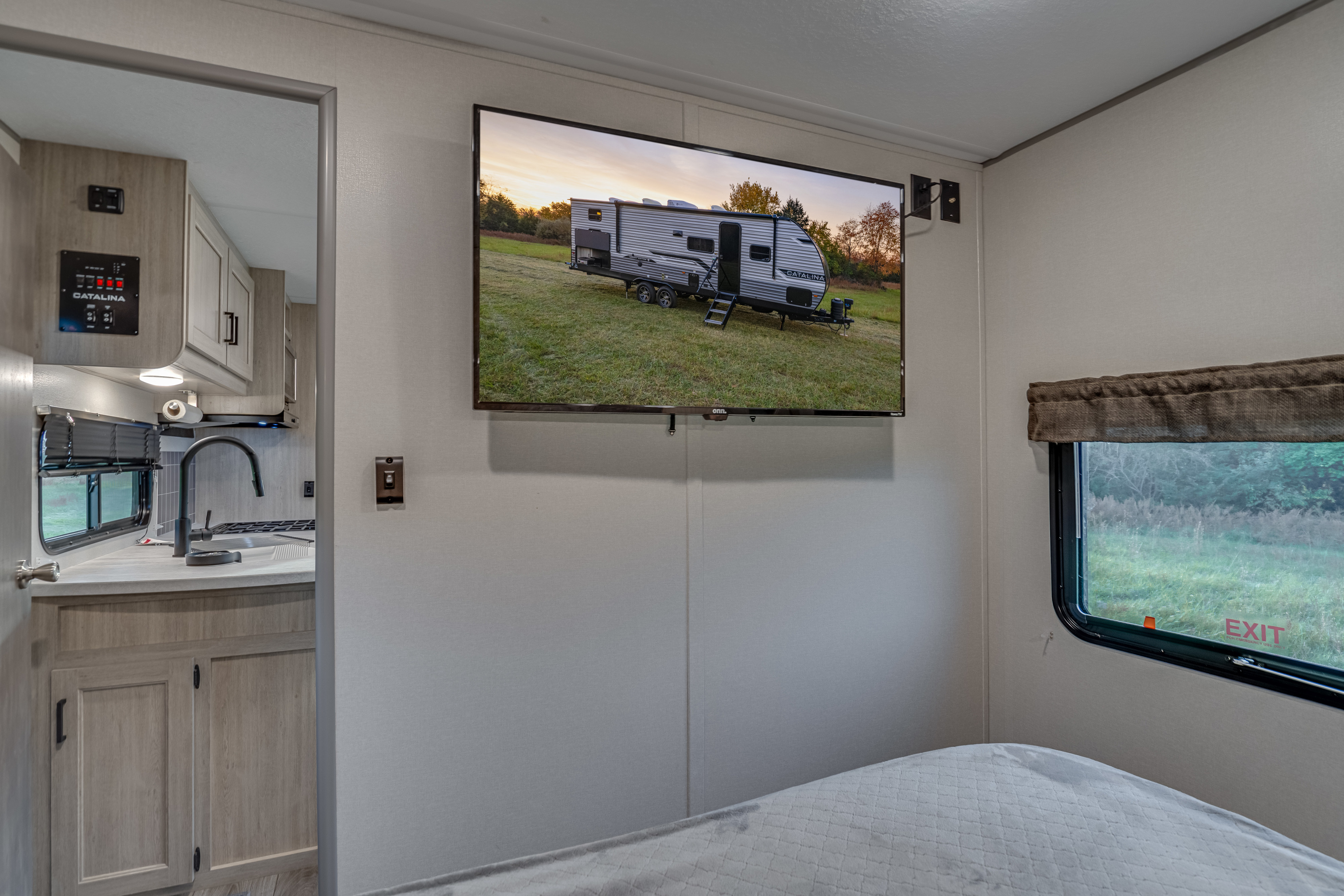 RV rental interior featuring a modern kitchen, large mounted TV showing an RV, and a comfortable sleeping area.. Coachmen Catalina Legacy 293qbck 2025