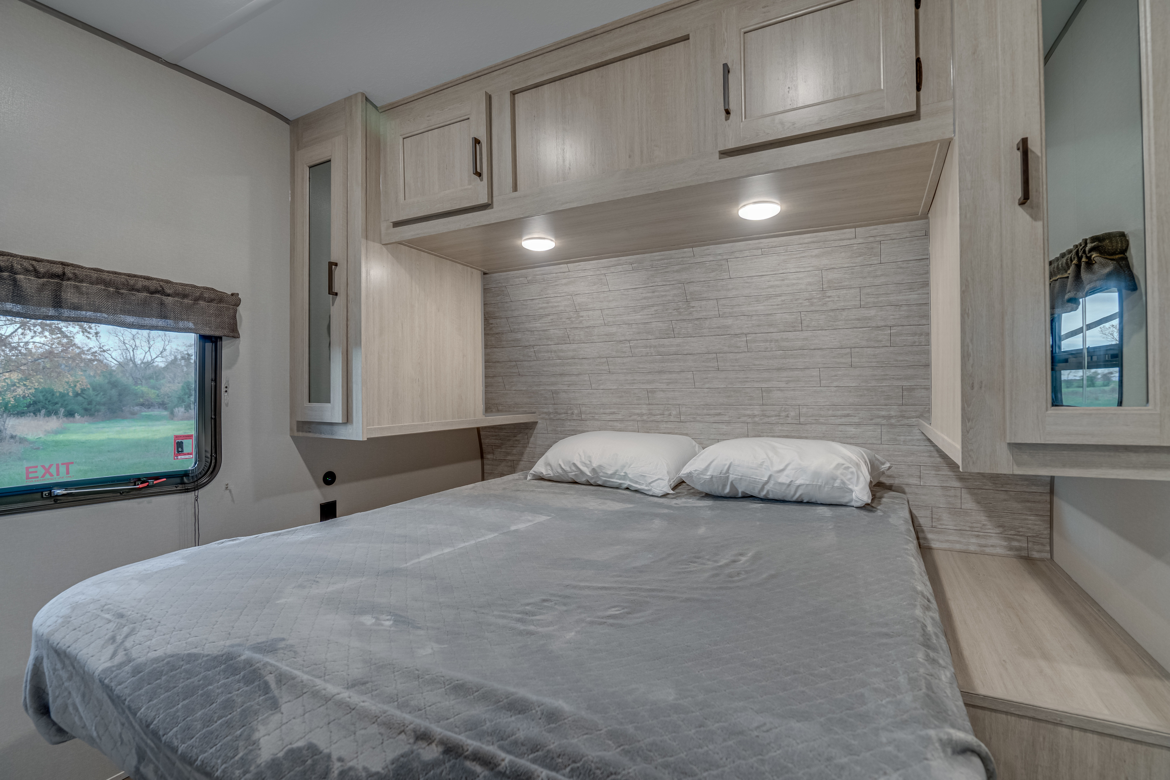 This modern RV rental bedroom features a comfy bed, overhead cabinets, and a window with a view of nature.. Coachmen Catalina Legacy 293qbck 2025