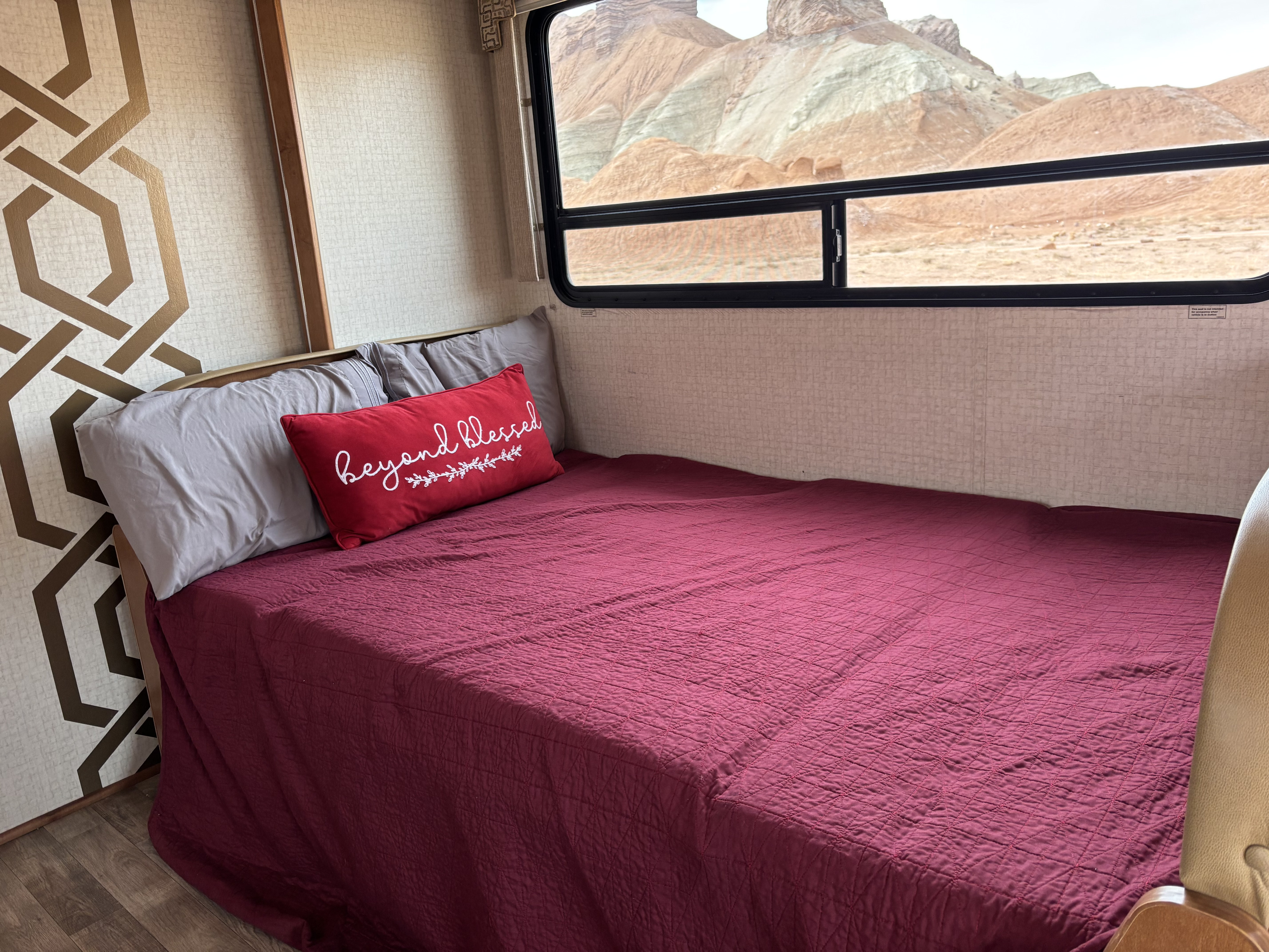 RV rental bedroom with scenic desert mountain views through the window, featuring a red quilt.. Winnebago Minnie Winnie 2017