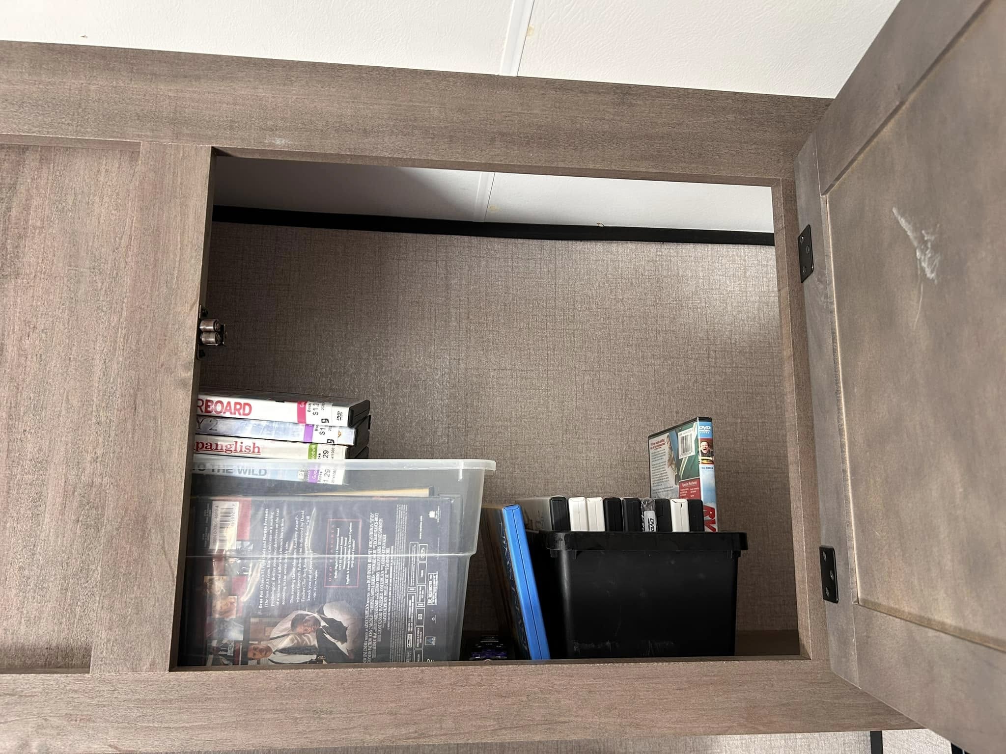 Inside an RV rental: An open overhead cabinet packed with DVDs, including "Seven" and "Panglish," and VHS tapes.. Highland Ridge RV Open Range 2022