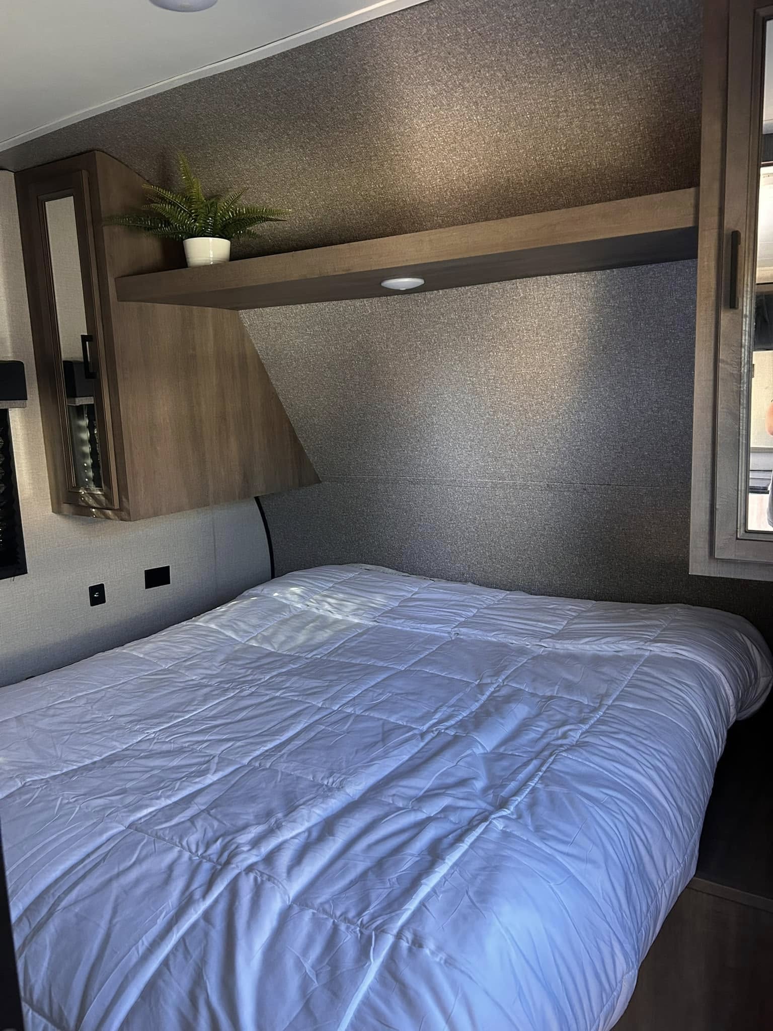 Modern RV rental bedroom features a comfy bed with white comforter, overhead storage, and plant decor.. Highland Ridge RV Open Range 2022