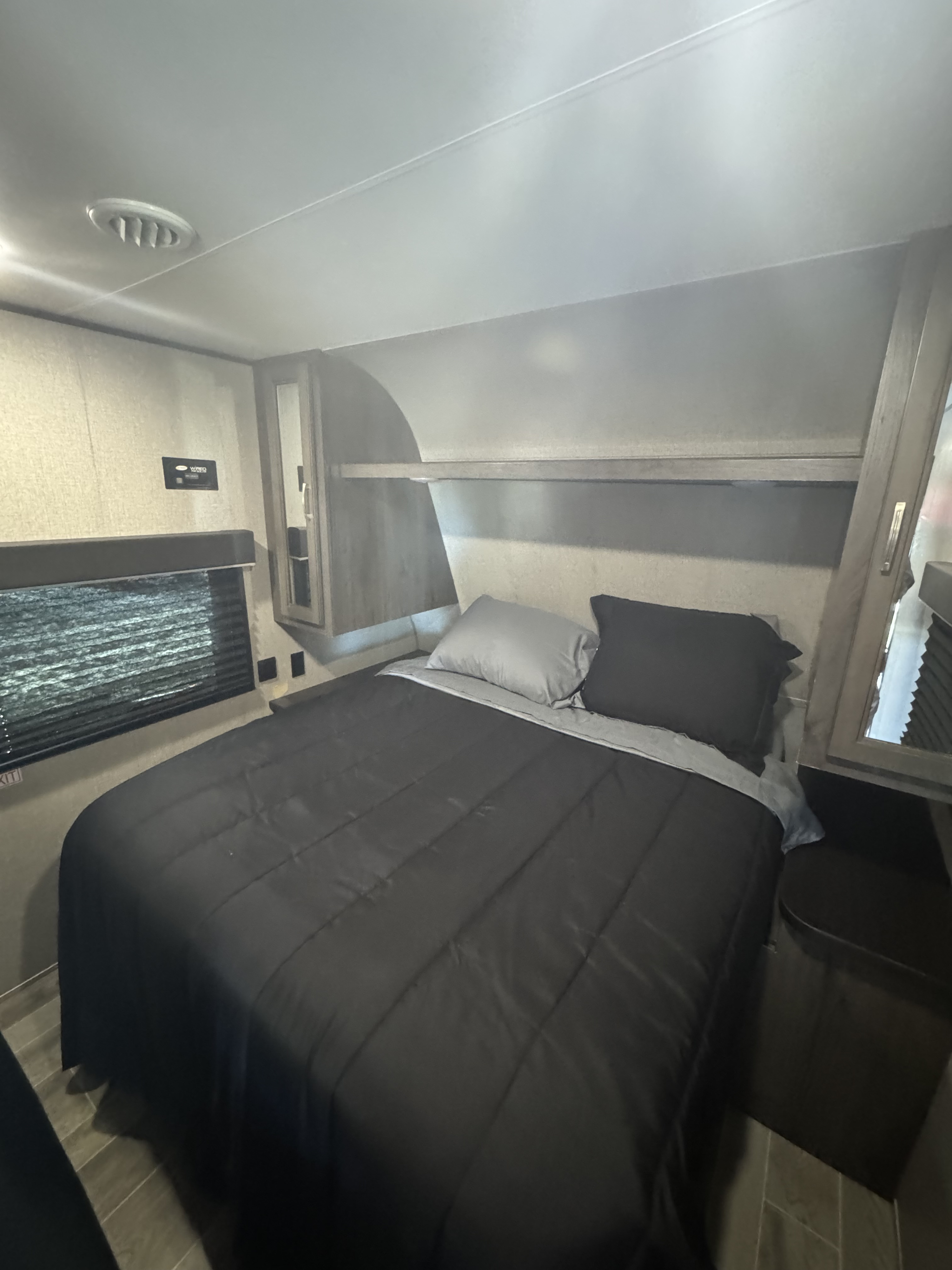 This compact RV rental bedroom features a comfy bed, window, and integrated storage, offering a cozy travel space.. Jayco Jay Flight SLX 2021