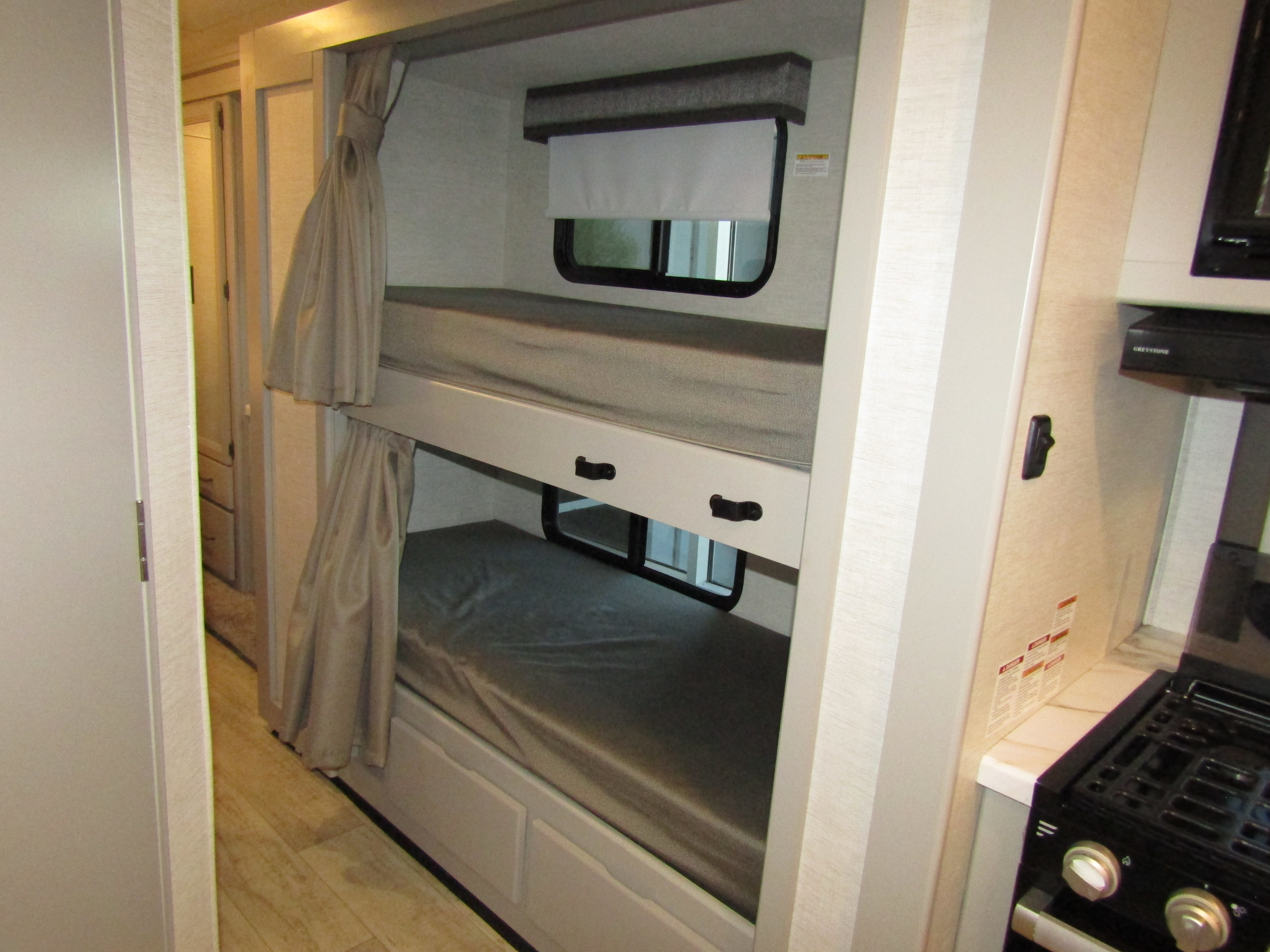 Inside an RV rental: two-tier bunk beds with individual windows and privacy curtains, plus a compact kitchen with a stove.. Thor Chateau 2024