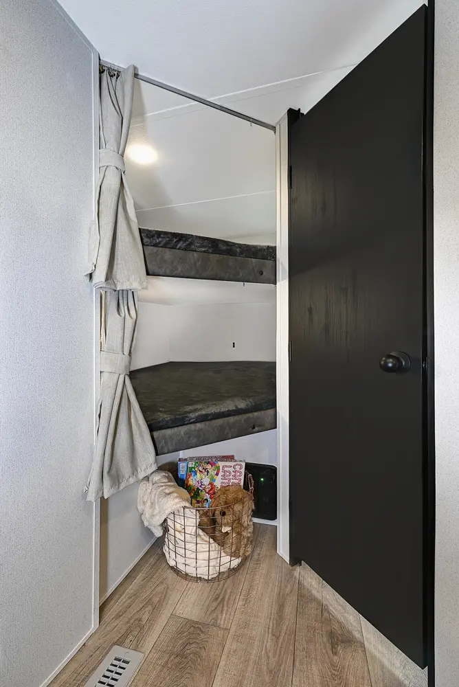 RV rental: Compact bunk beds with tied-back curtains. Floor features a basket with books/toys and an electronic device, ideal for family stays.. Palomino Puma 283BHCE 2025