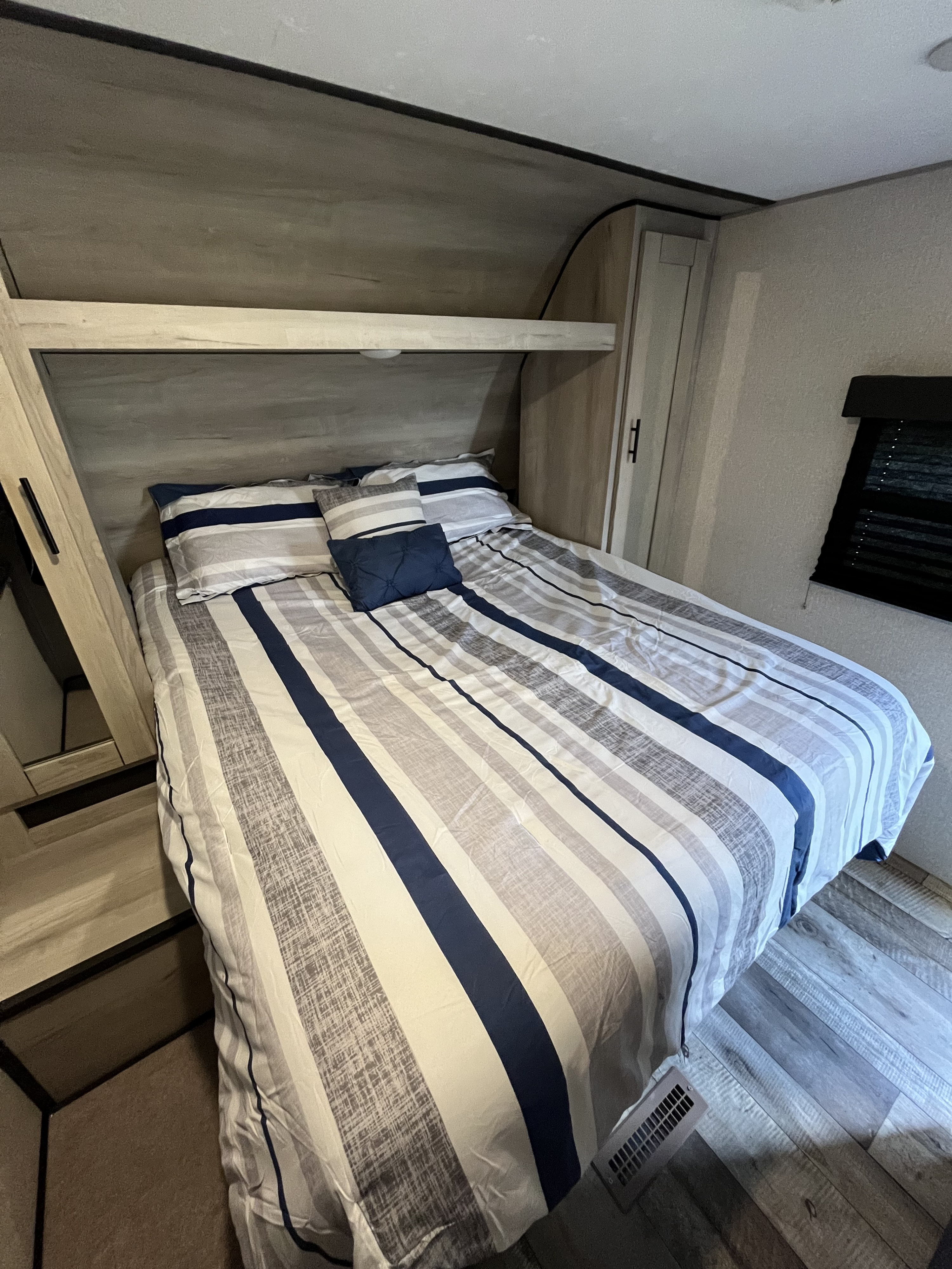 Cozy RV rental bedroom with a large bed, blue and grey striped bedding, built-in storage, and light wood-look floor.. KZ Connect 2021