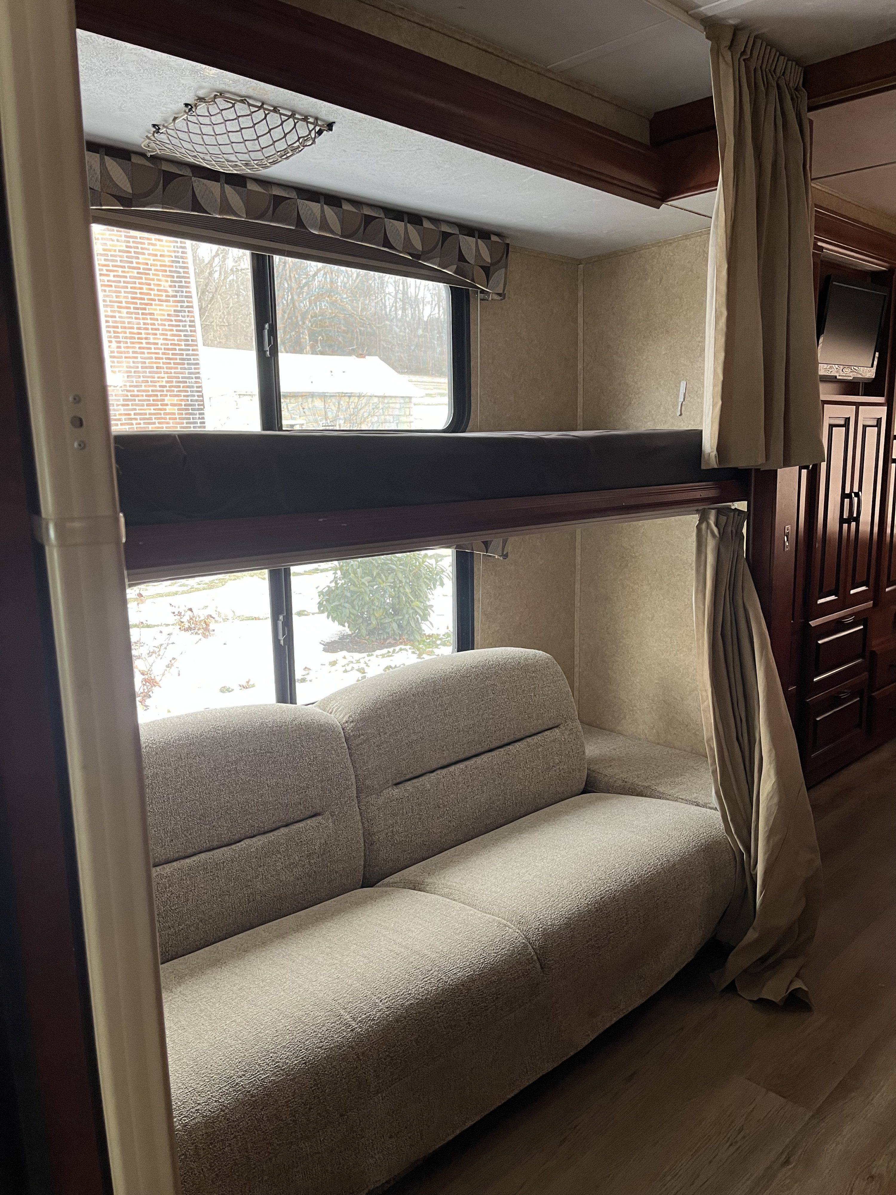 Cozy rv rental interior: lower bunk transforms into a sofa, upper bunk bed, and large windows revealing a snowy view.. Forest River Sunseeker 2013
