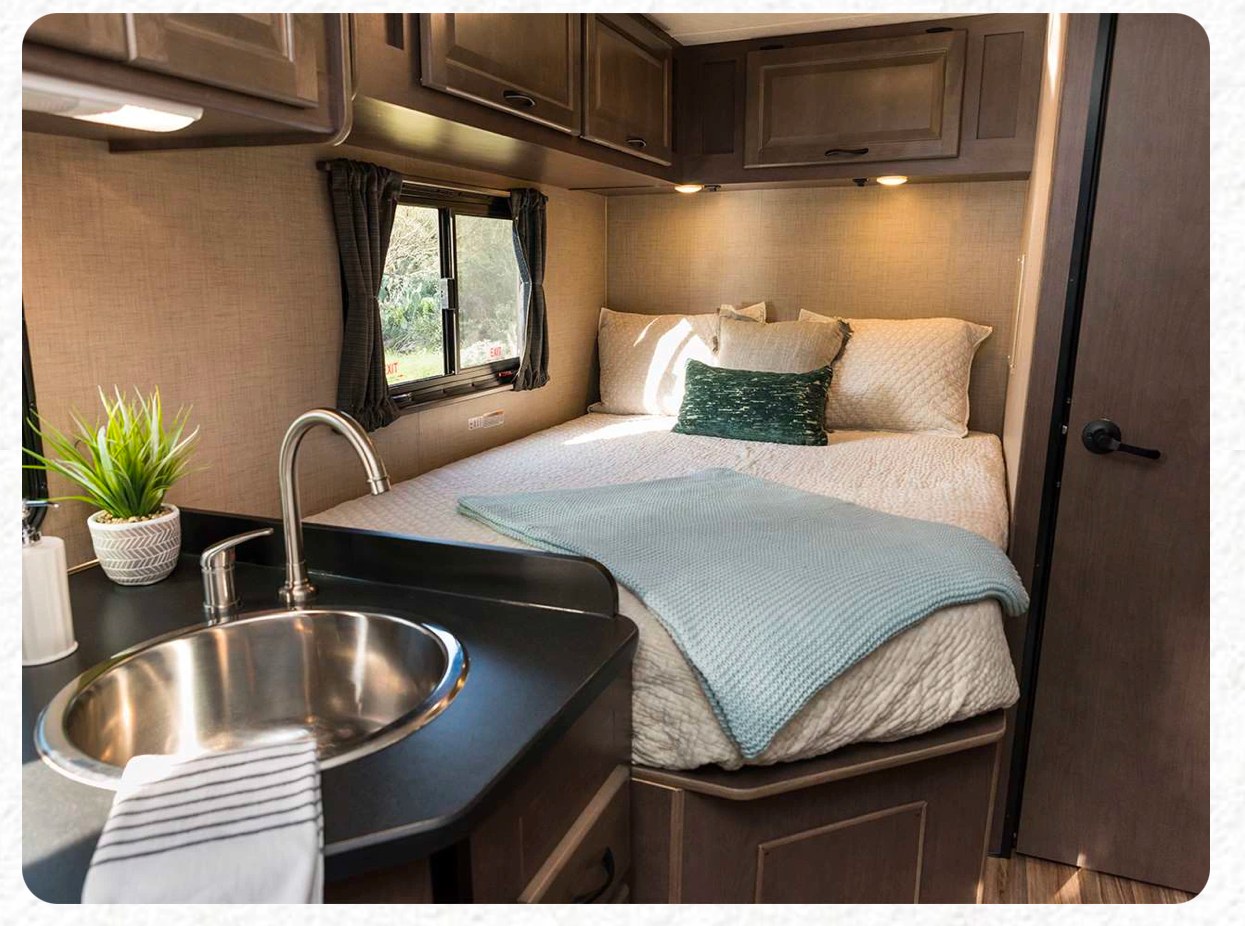 RV rental interior: A cozy bedroom setup with a comfortable bed, small kitchen sink, and overhead storage cabinets.. Thor Majestic 2019