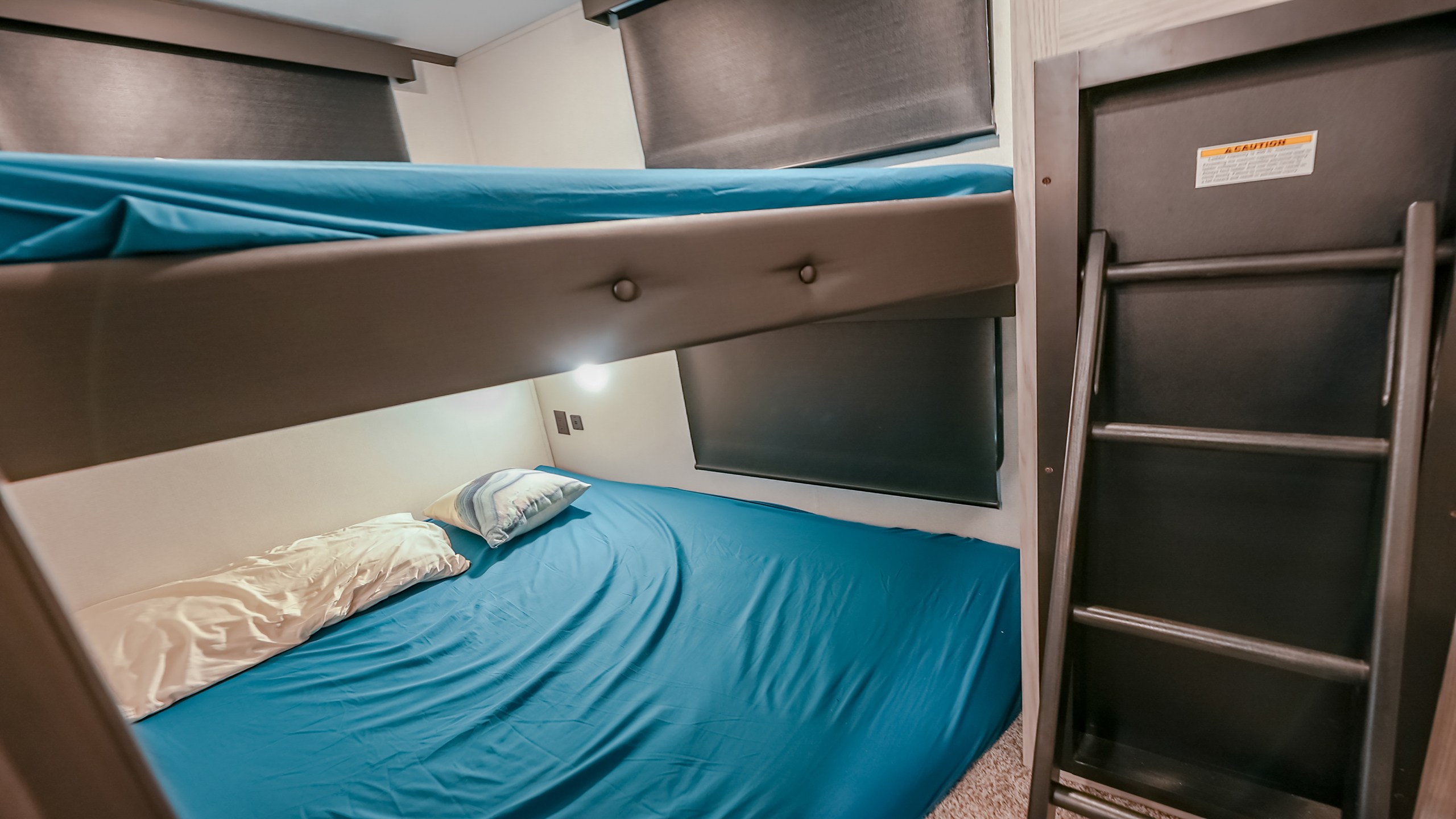 An RV rental's sleeping area with blue bunk beds, upper and lower bunks, and a ladder, designed for compact travel.. Keystone Montana High Country 2021