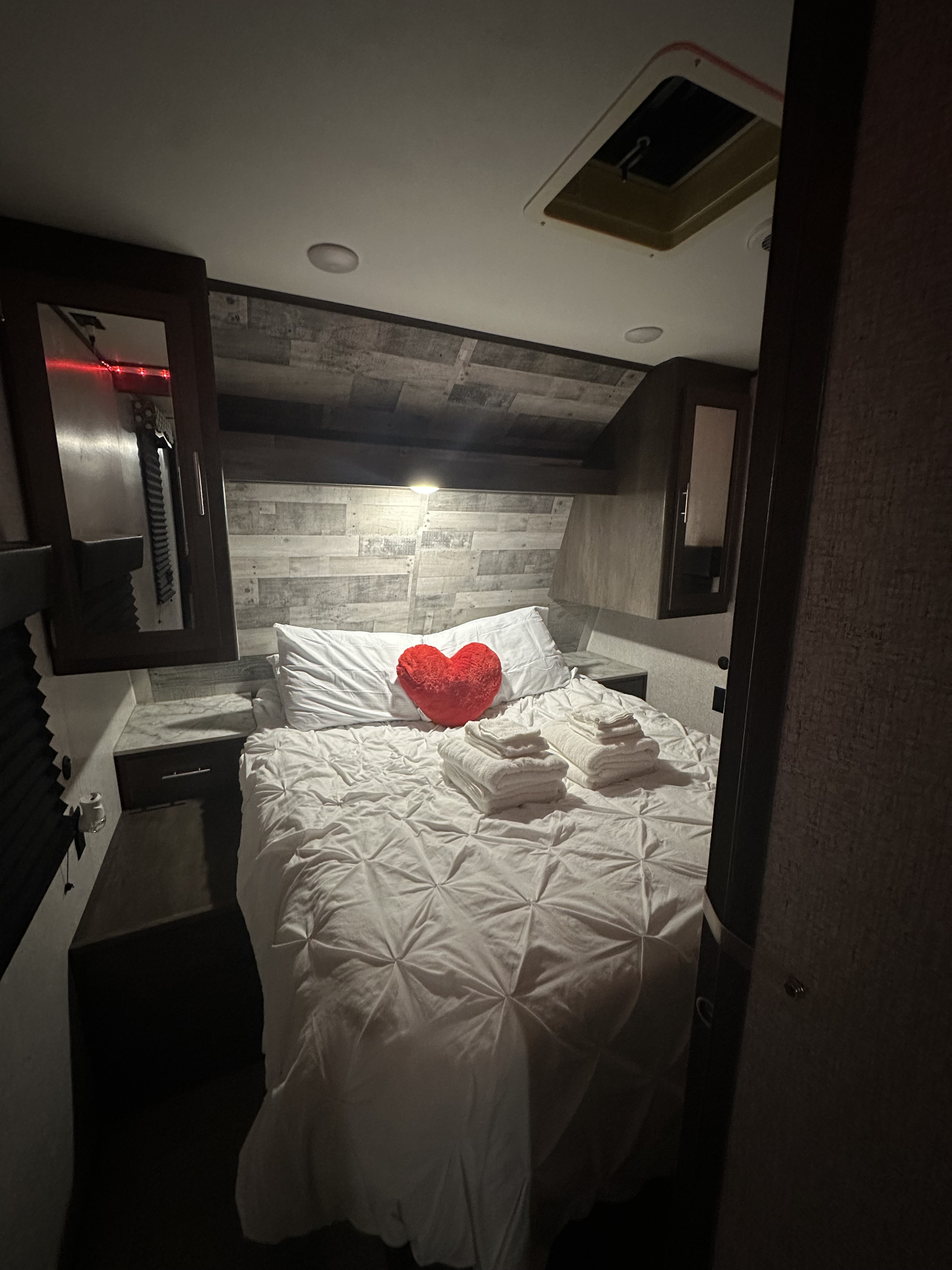 Cozy RV rental bedroom with white linen bed, red heart pillow, and folded towels, perfect for a comfortable stay.. Coleman CM337BH21 2021
