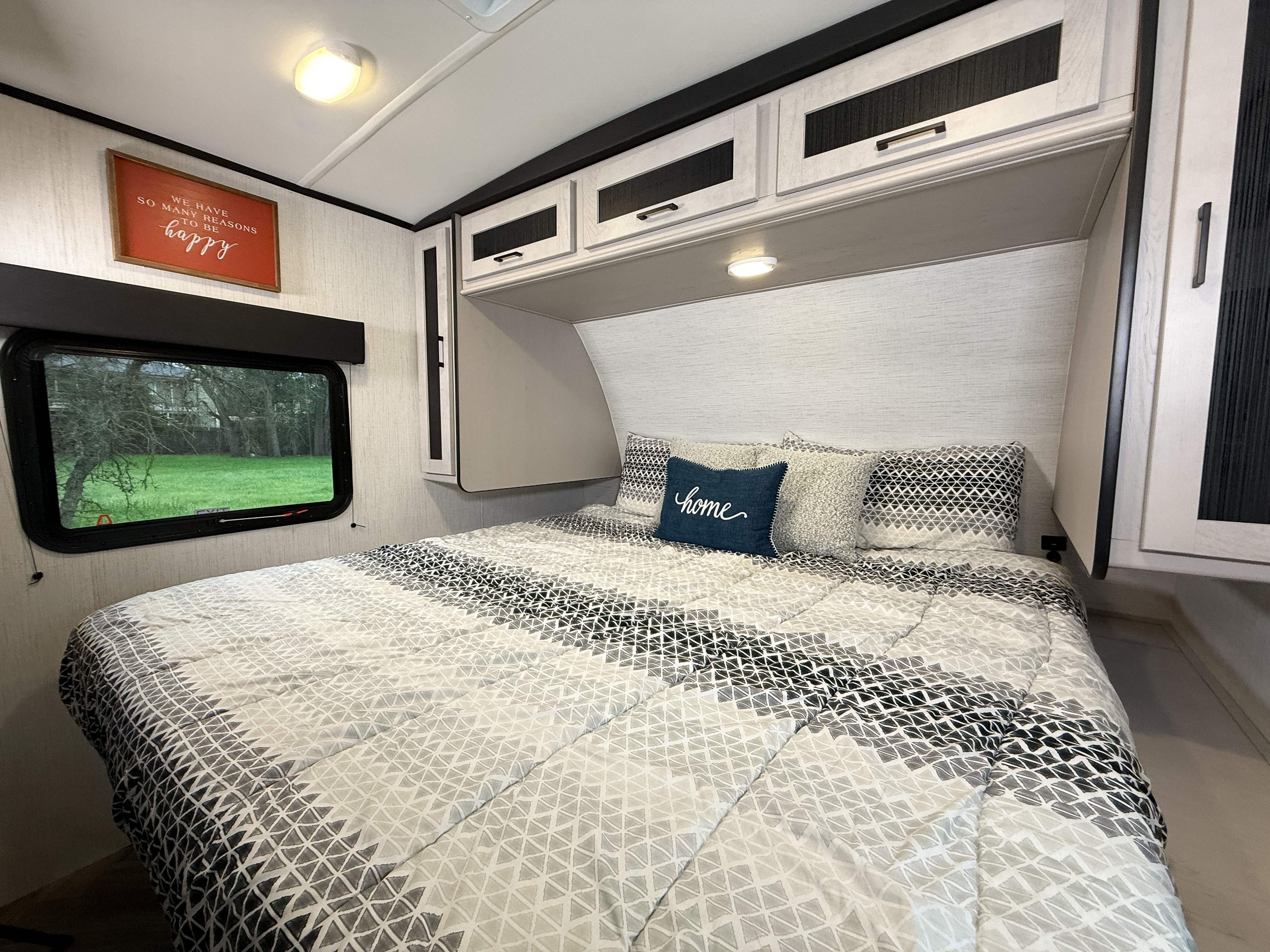 RV rental bedroom featuring a patterned bed, light-toned cabinets, and a window looking out to a green landscape.. Heartland mallard 2023