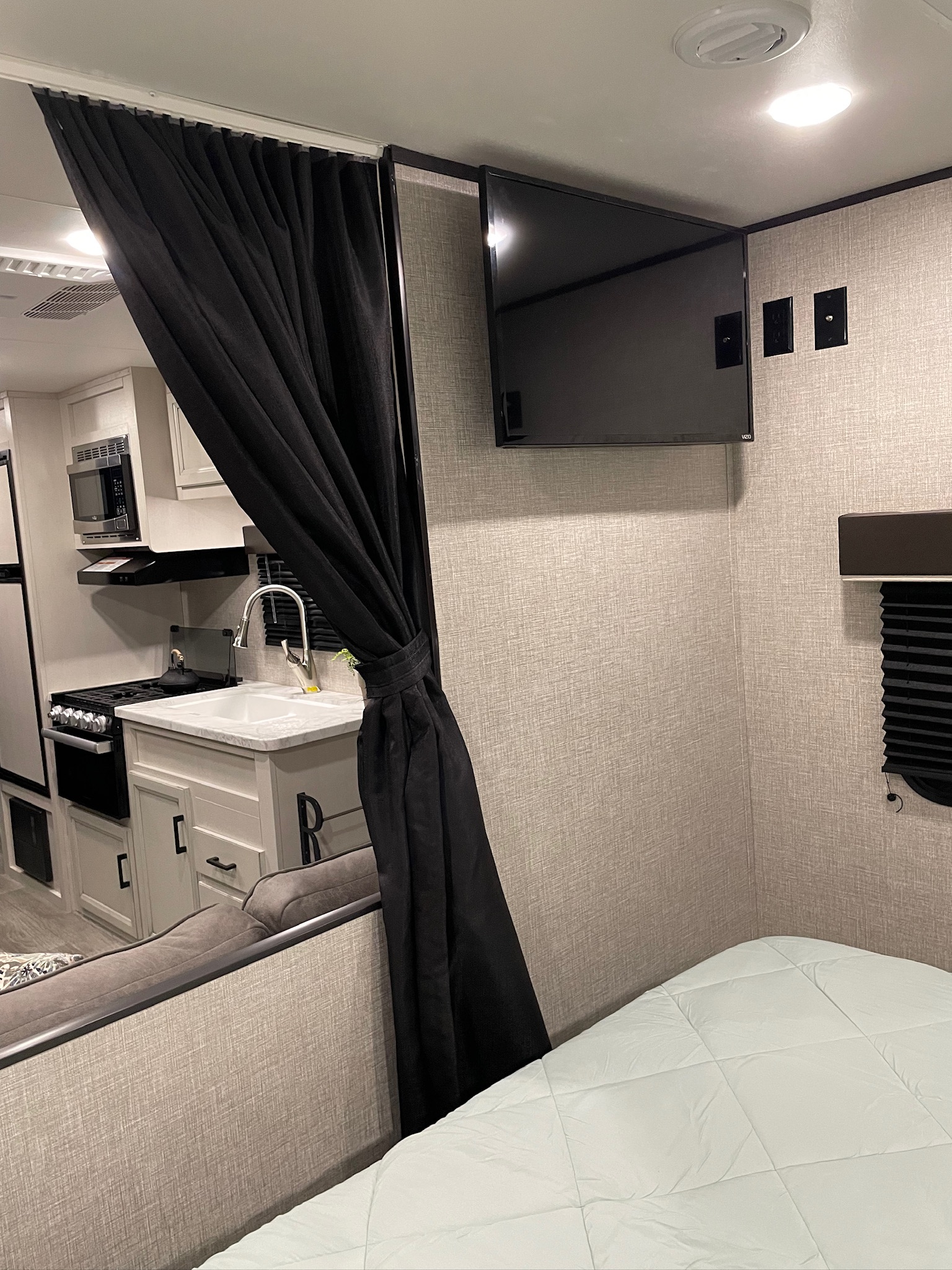 Explore this cozy RV rental interior, showcasing a compact kitchen, private curtain, mounted TV, and comfortable sleeping area.. Jayco Jay Flight SLX 2022