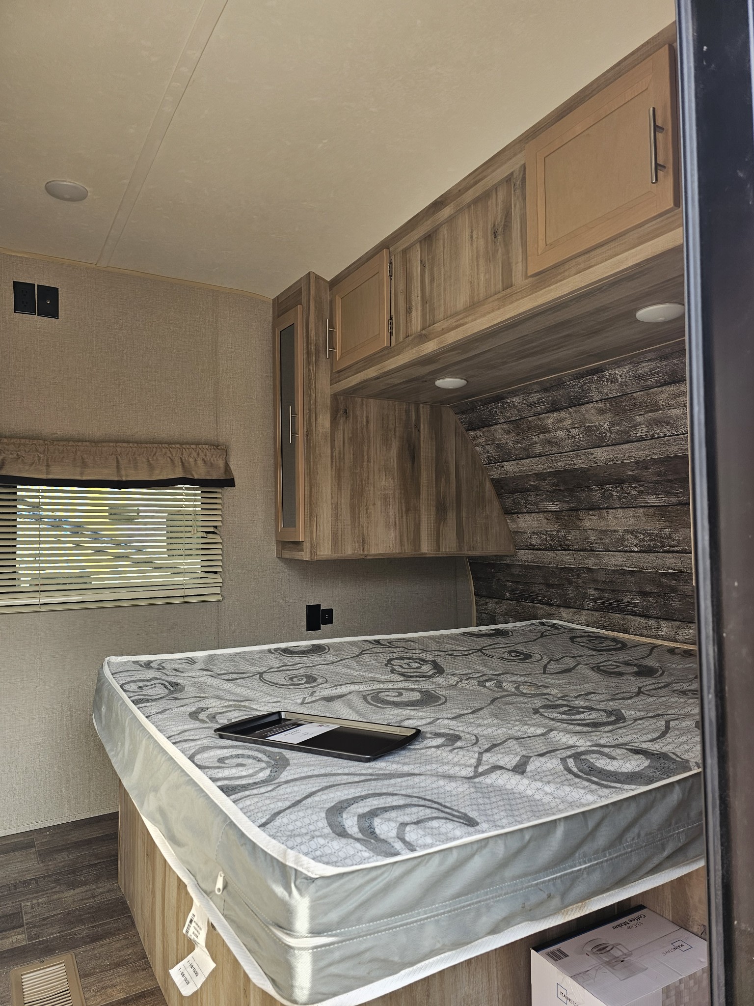This RV rental interior shows a cozy bedroom with a patterned mattress, wood-look cabinets, and window.. Forest River Catalina 2020