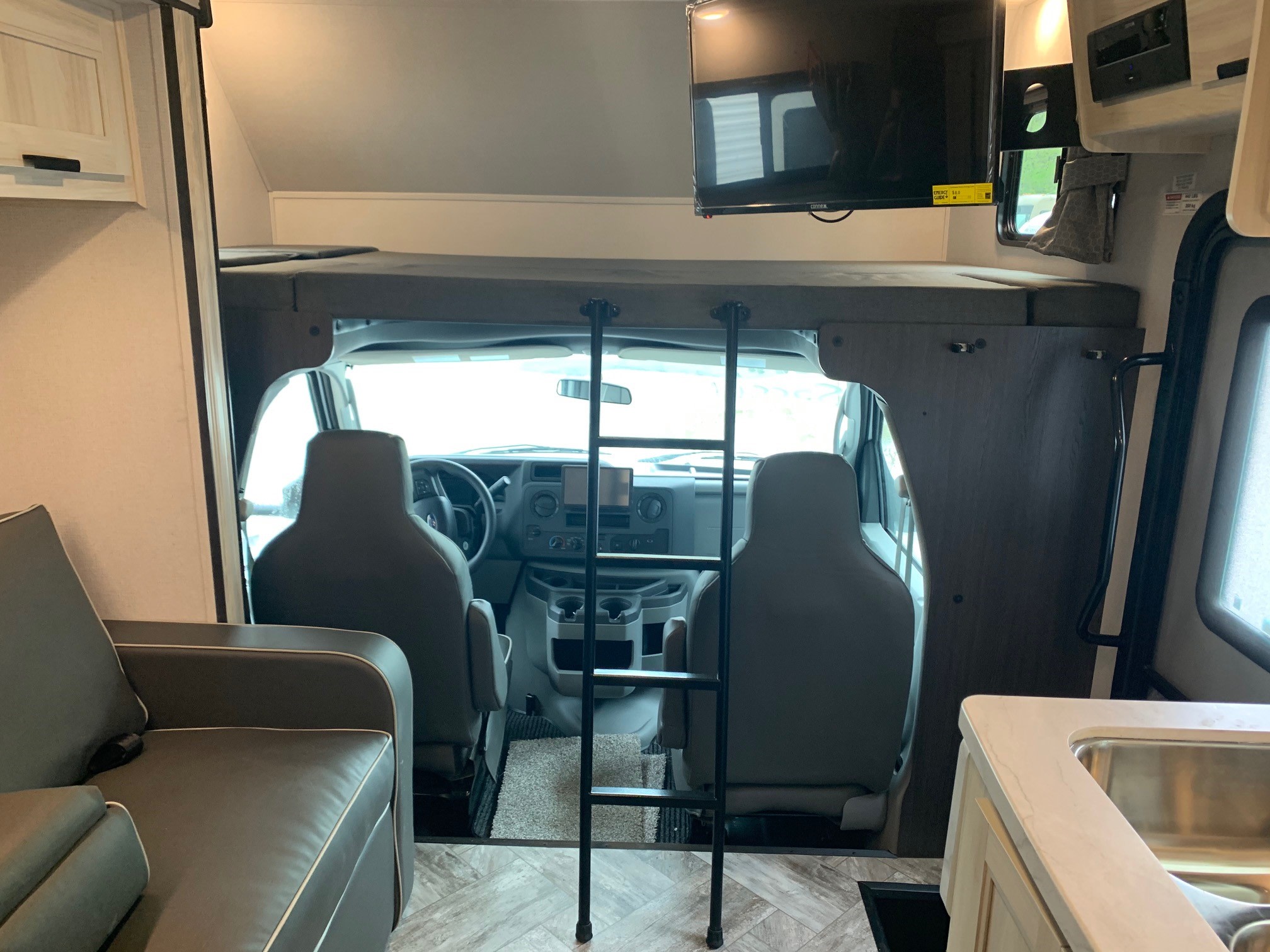 Cozy RV rental interior: view of cab, bunk bed with ladder, TV, sofa, and kitchen counter.. Forest River Sunseeker 2026