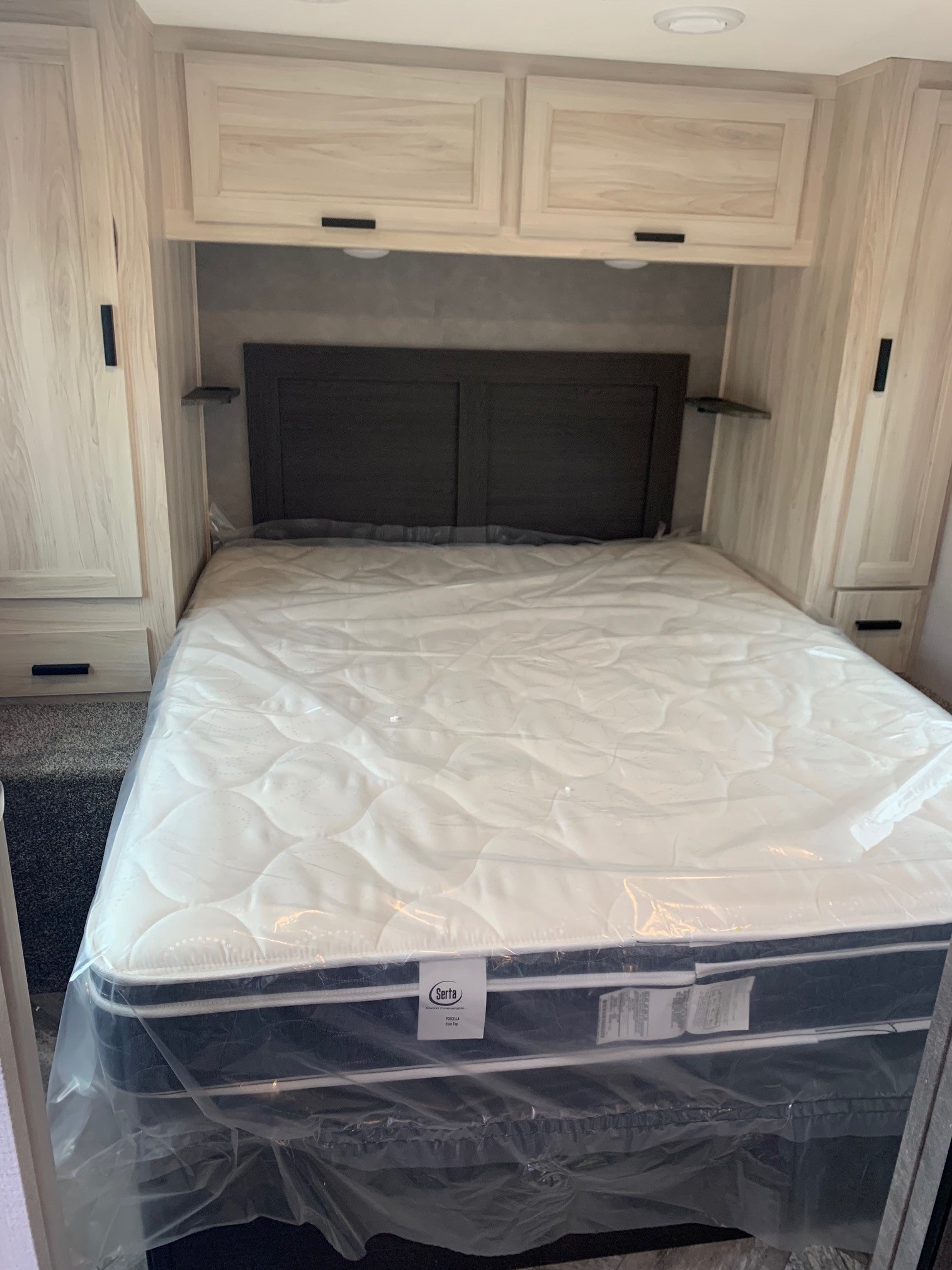 New RV rental bedroom with Serta mattress in plastic, light wood cabinets, and headboard.. Forest River Sunseeker 2026
