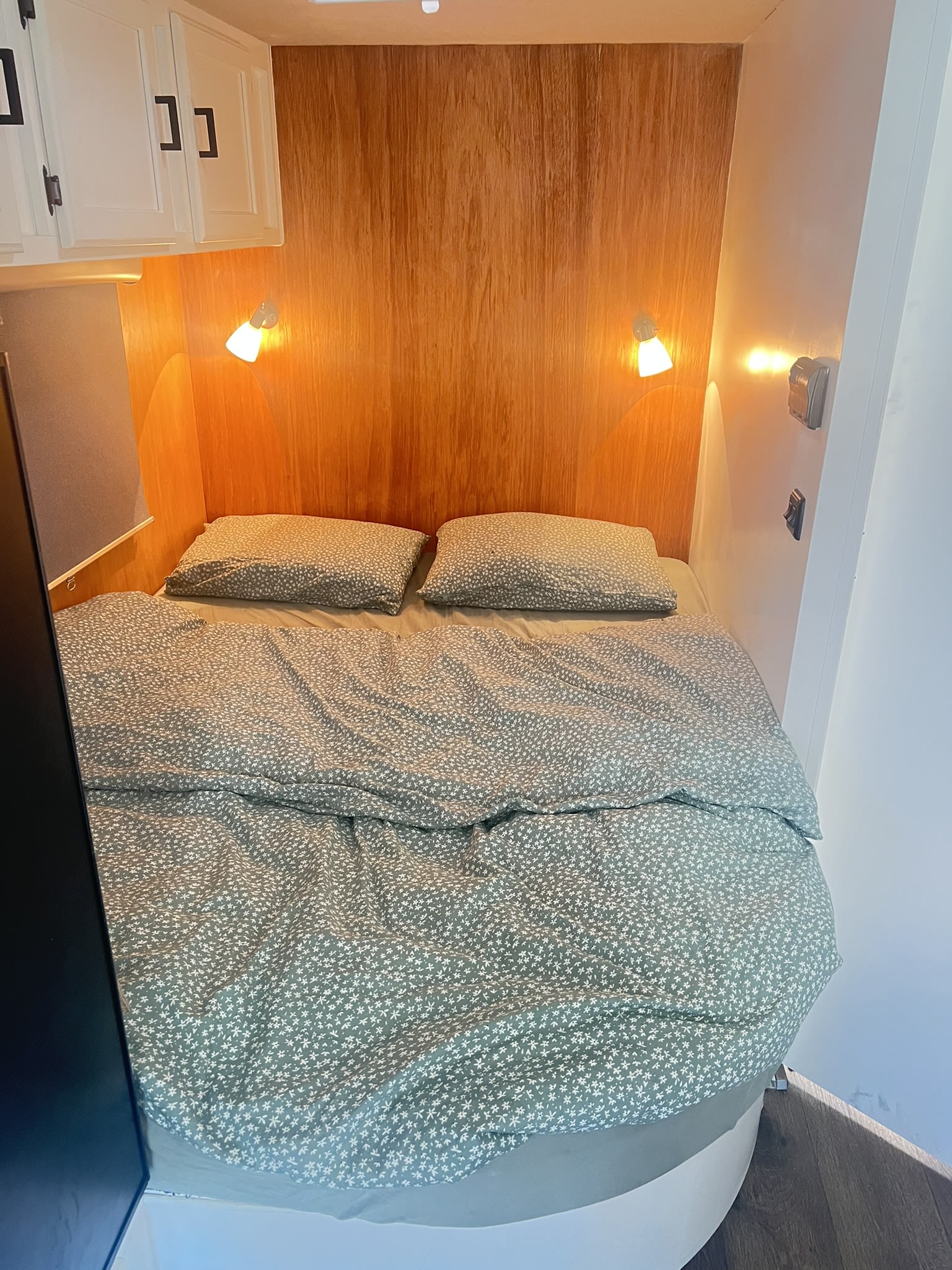 Cozy RV rental bedroom: a comfortable bed with green floral bedding, warm wood paneling, and wall-mounted reading lights.. Adventurer Adventurer Motorhome 2016