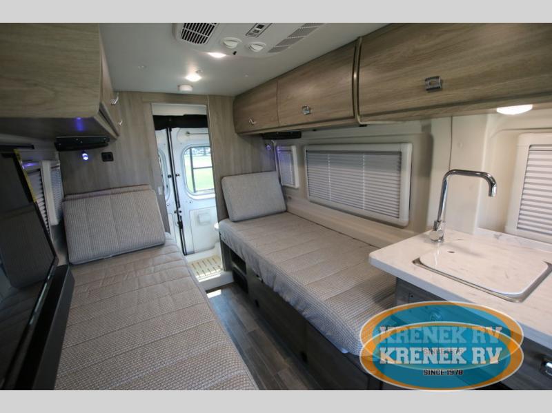 RV rental interior featuring convertible twin beds, a compact kitchen sink, and overhead storage in a modern camper van.. Winnebago Travato 2022